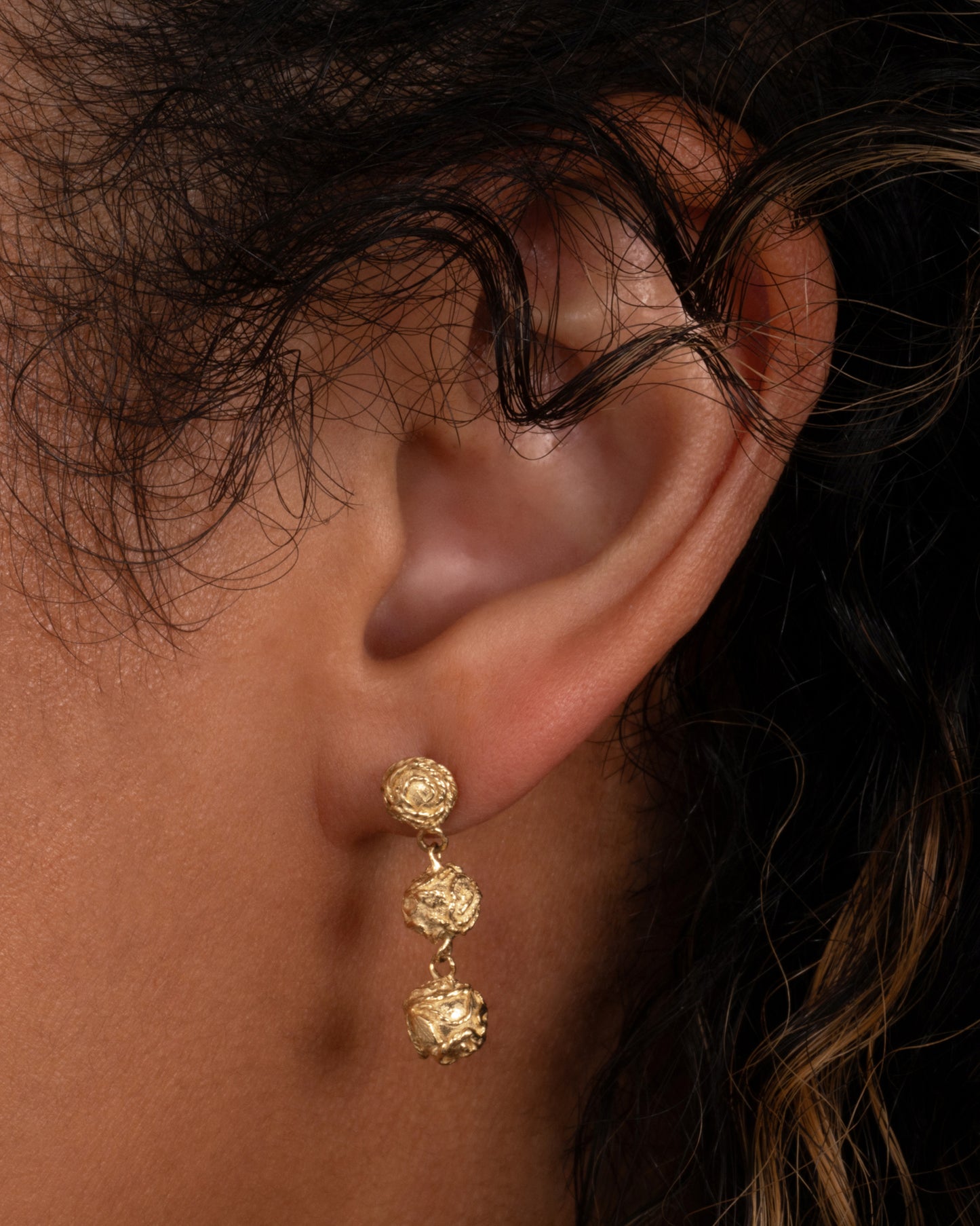 A pair of yellow gold dangle earrings with three linked spheres. Shown worn in an ear.