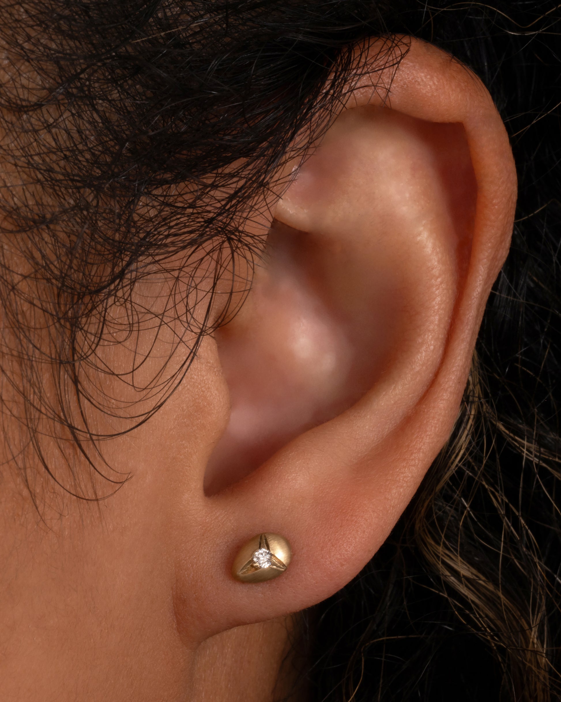 Yellow brushed gold teardrop shaped earrings with white diamonds at the center. Shown worn in an ear.