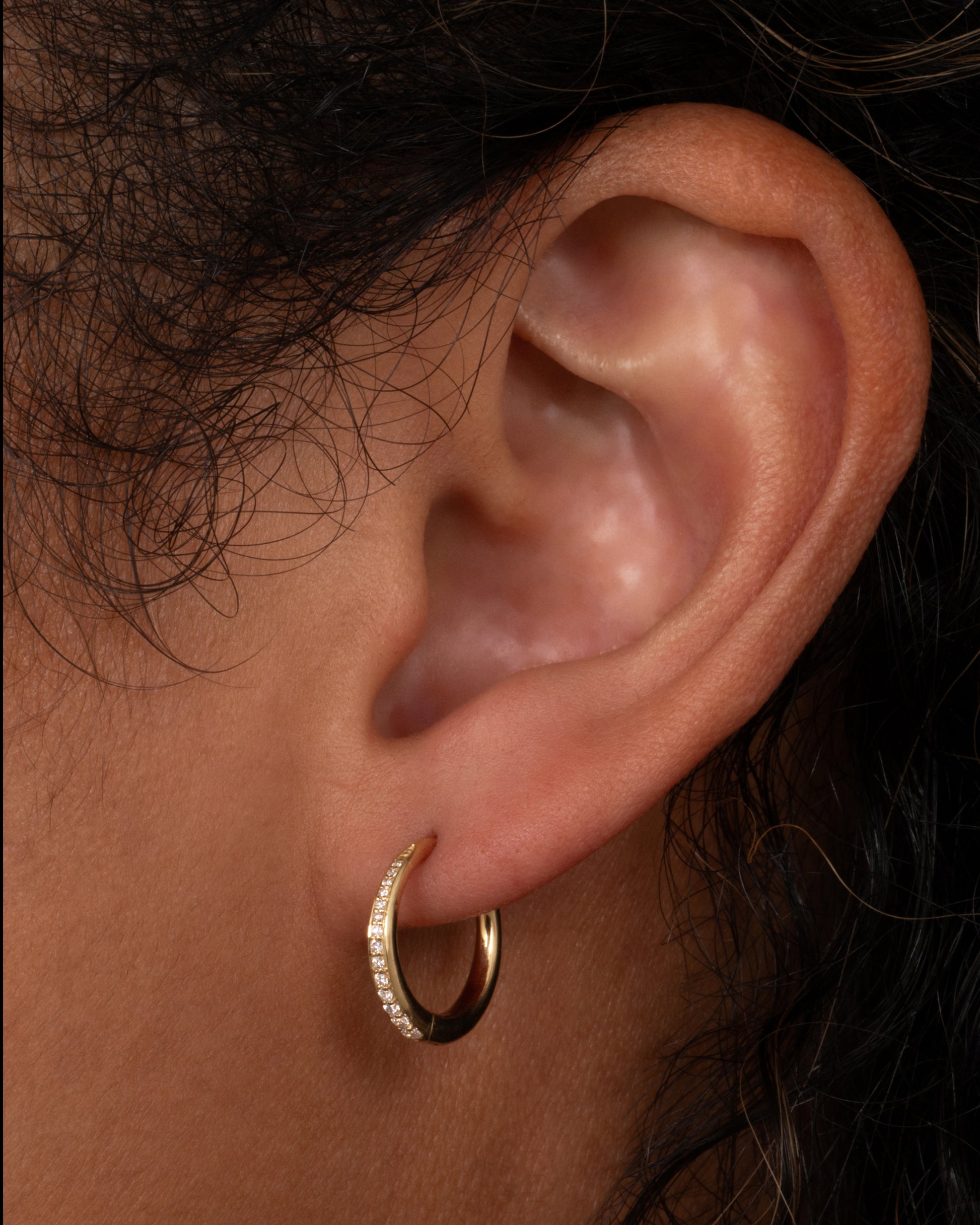 A yellow gold tapered hoop with a queue of graduated diamonds. Shown on an ear.