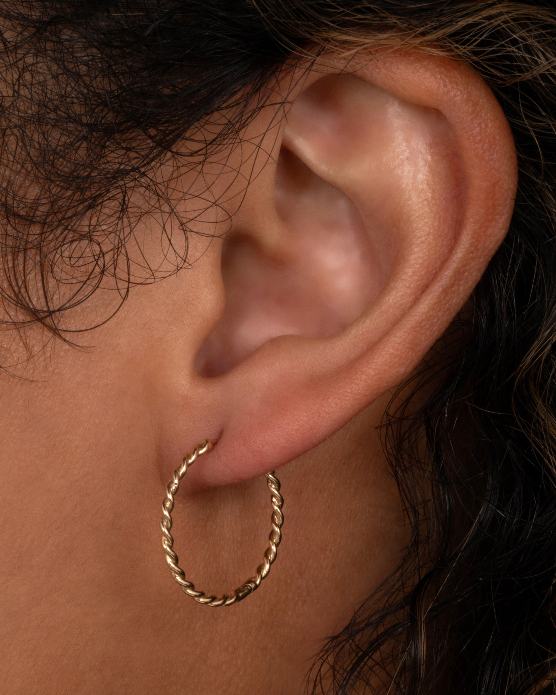 A yellow gold twisted hoop earring with a clicker clasp, shown on an ear.