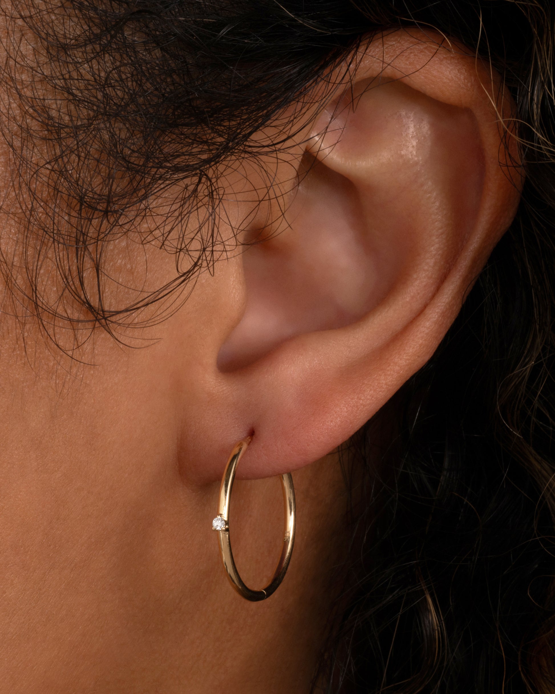 A yellow gold hoop earring with a tiny prong set diamond, shown on a person.