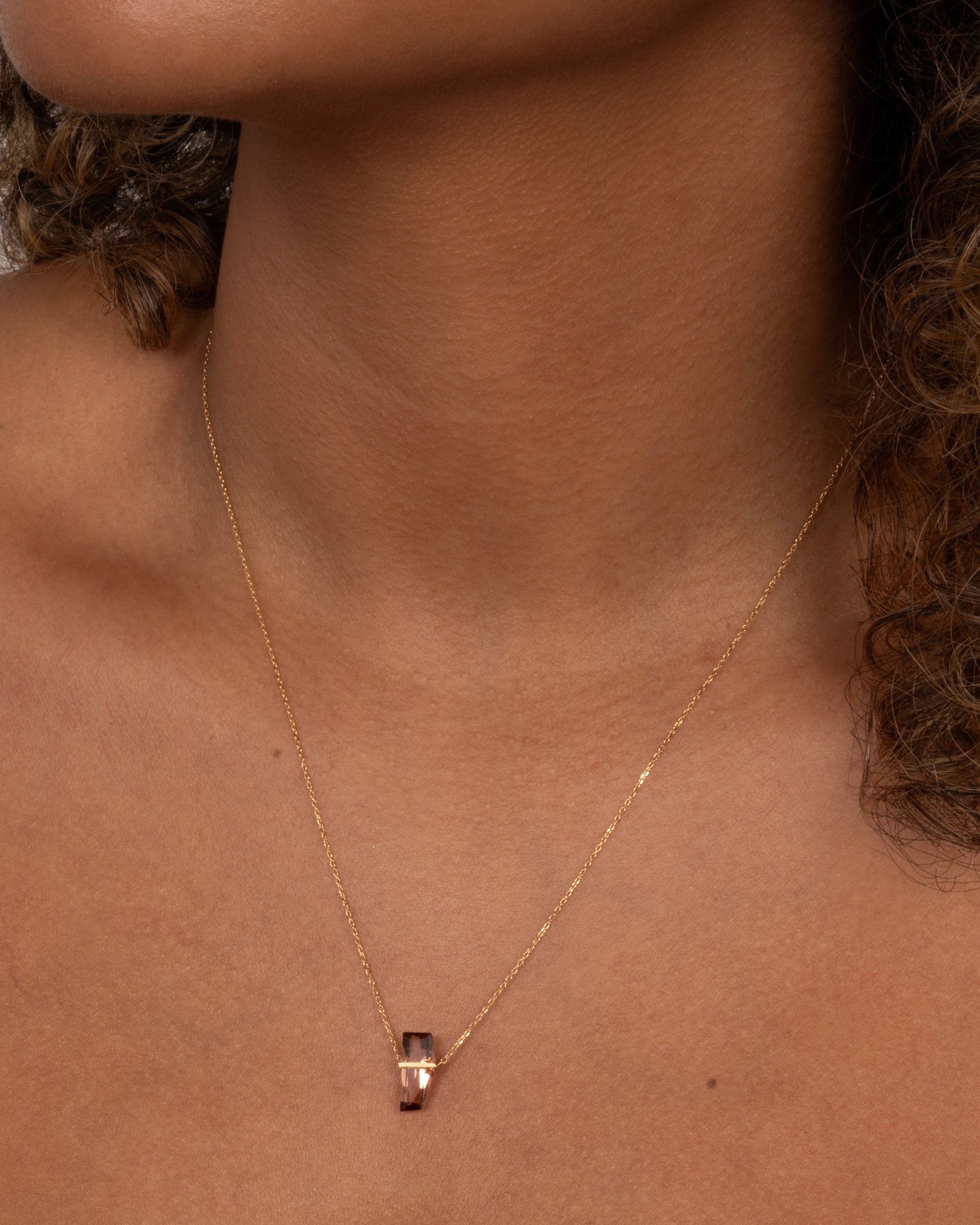A yellow gold cable chain necklace with a five sided rosy quartz in an open bar setting. Shown from the front on a person.
