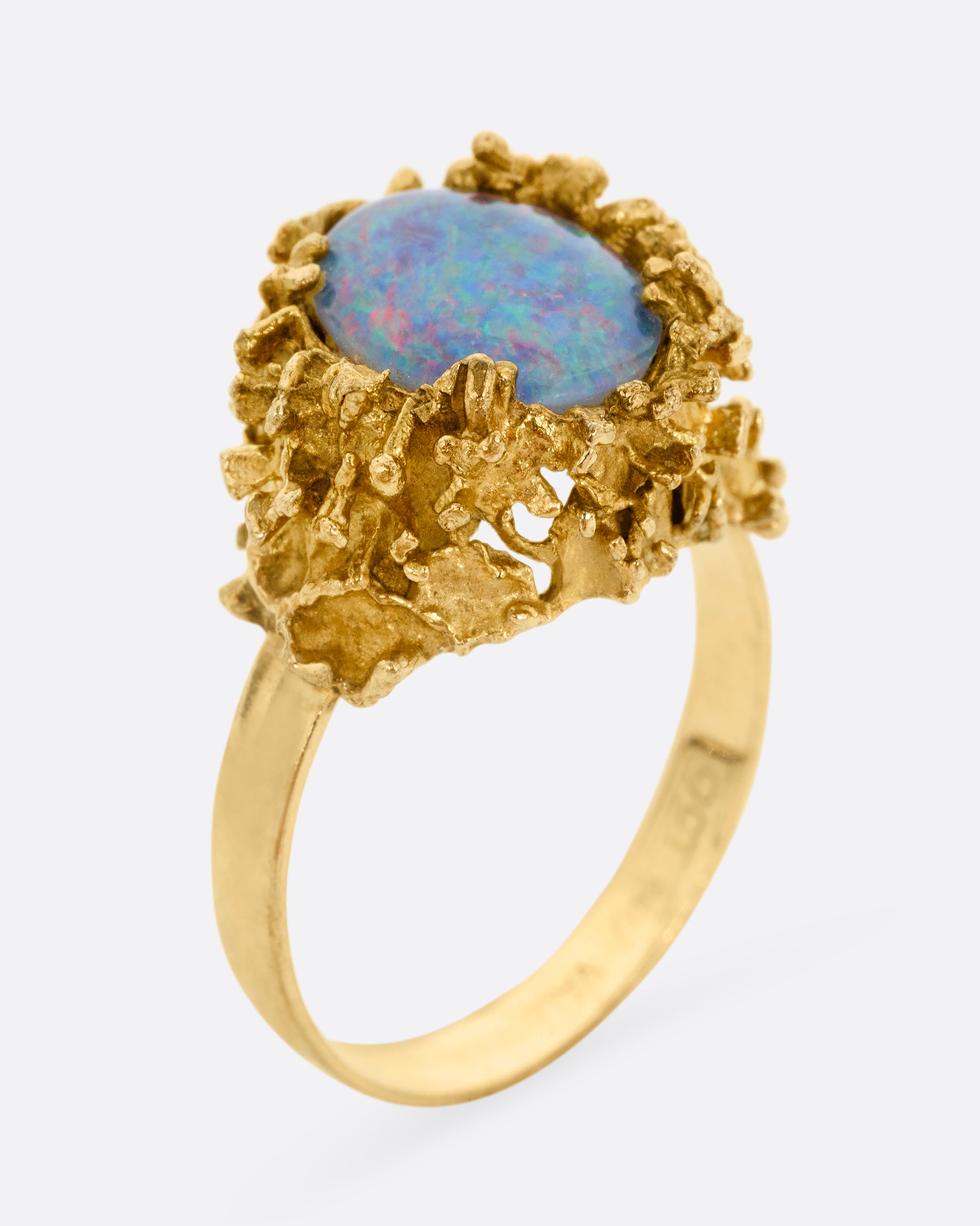 A yellow gold Brutalist era statement ring with an opal doublet in a molten gold nest. Shown standing up from the side.