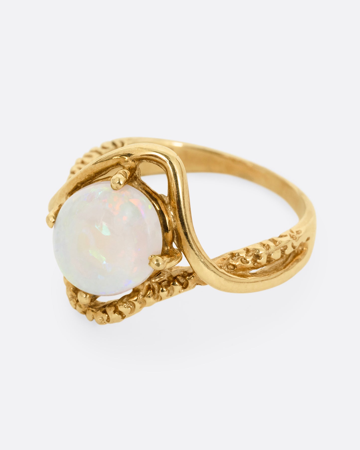 A yellow gold ring with two contrasting bands of polished and textured gold with an oval opal at the center. Shown from the side.