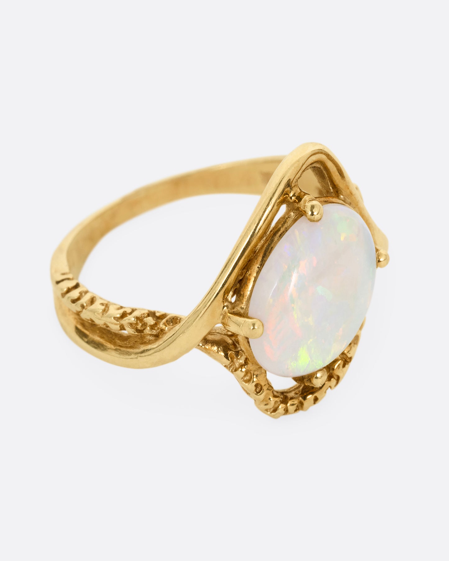 A yellow gold ring with two contrasting bands of polished and textured gold with an oval opal at the center. Shown from the side.