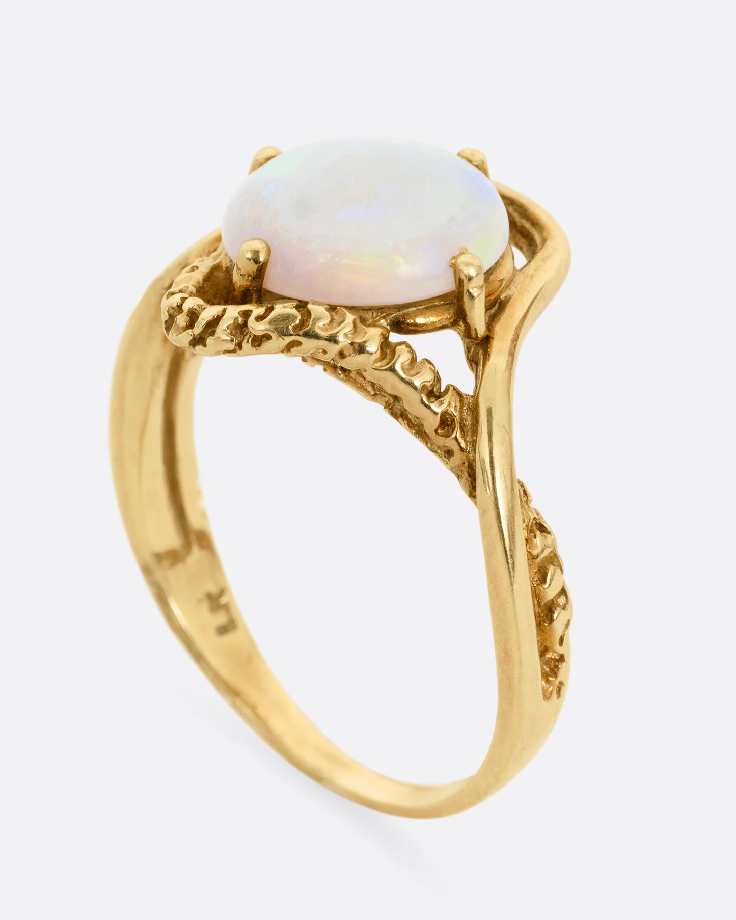 A yellow gold ring with two contrasting bands of polished and textured gold with an oval opal at the center. Shown standing up from the side.