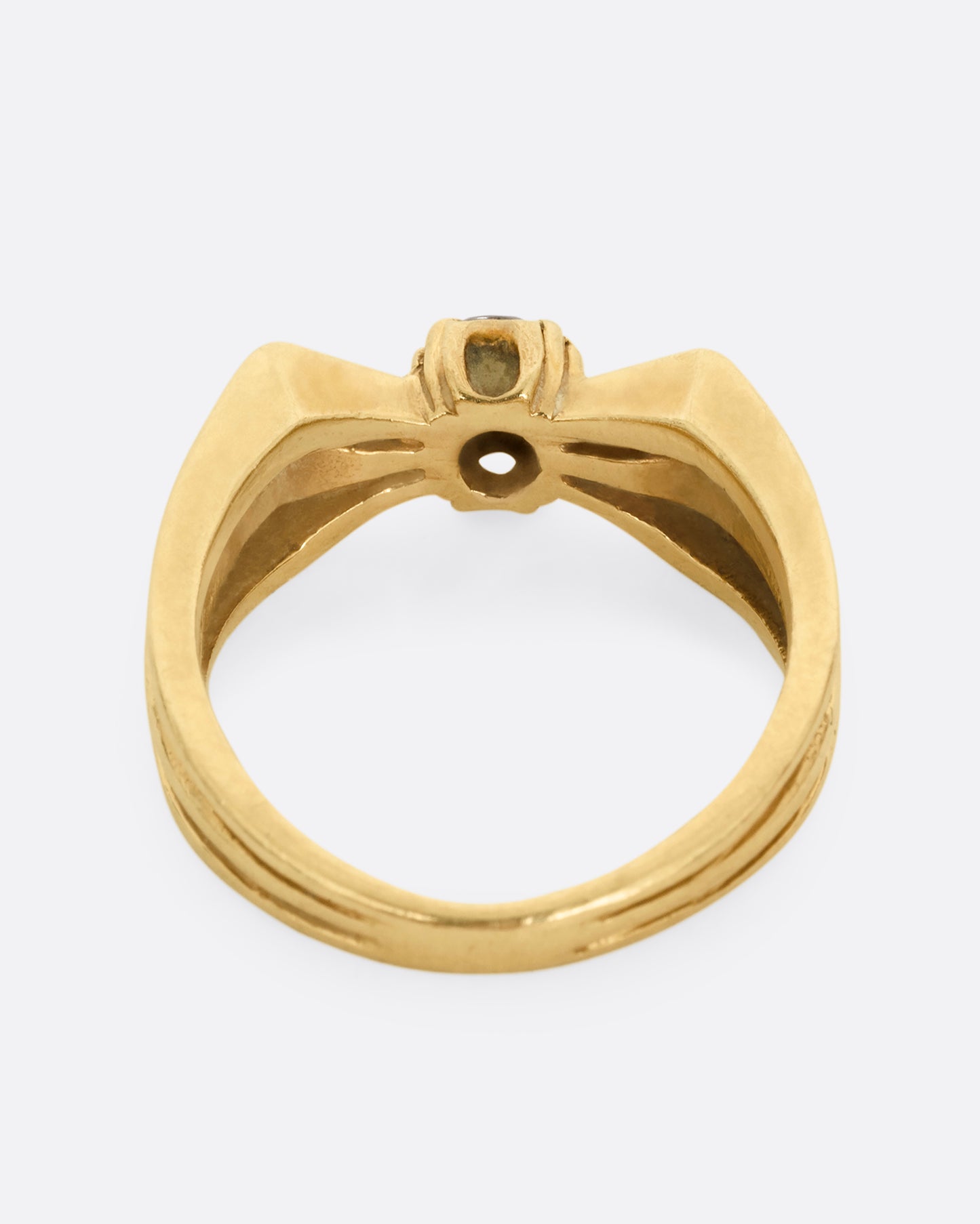 A yellow gold ring with a stacked silhouette and angular shoulders and a prong set diamond at the center. Shown from the back.