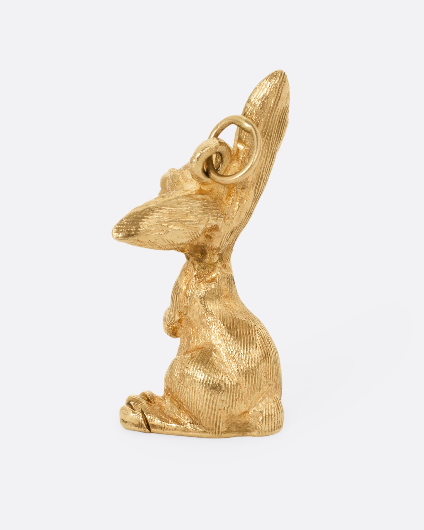 A yellow gold rabbit charm with one ear perked, sitting up. Shown from the back.
