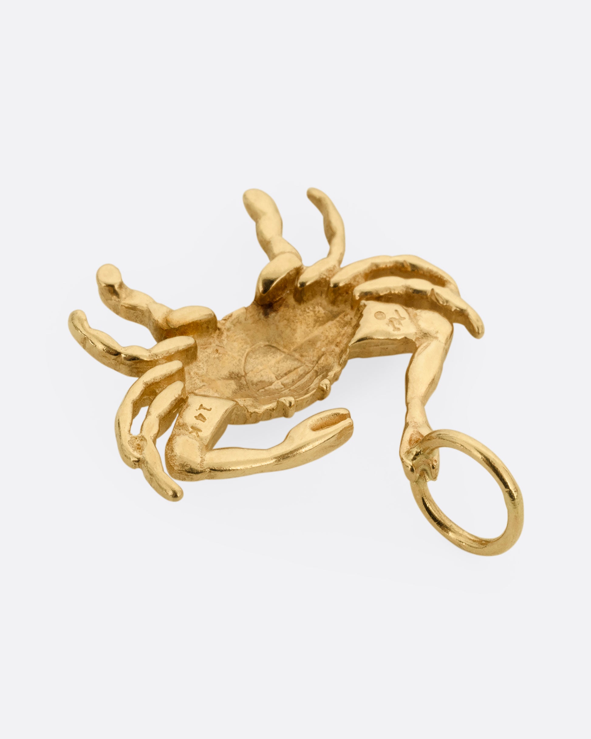 A yellow gold crab pendant grasping onto a jump ring with one claw. Shown from the back.
