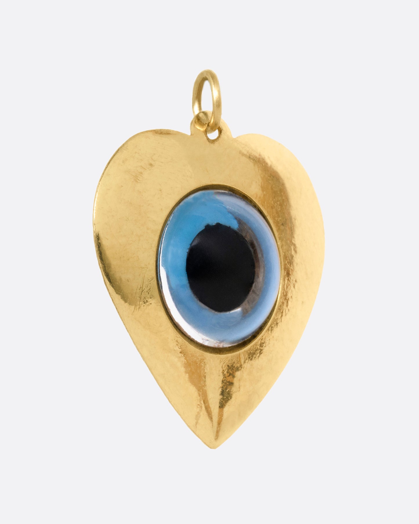 A yellow gold heart shaped charm with an evil eye at its center. Shown from the side.