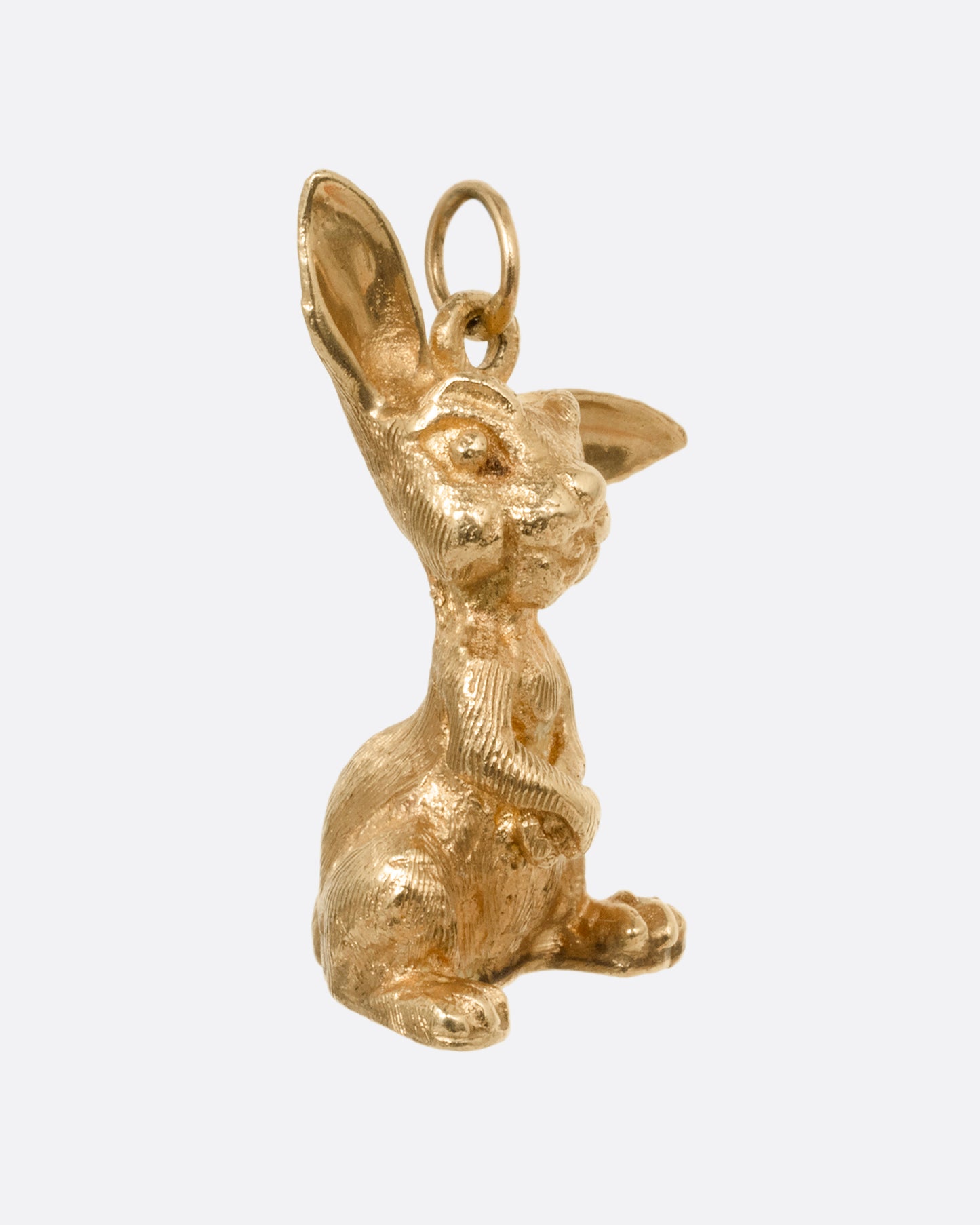 A yellow gold rabbit charm with one ear perked, sitting up. Shown from the side.