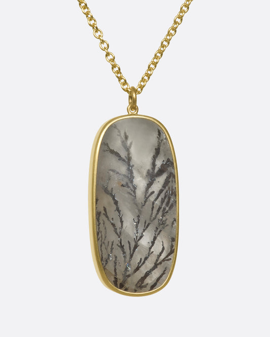 A close up of a hanging dendritic quartz pendant on a yellow gold chain.