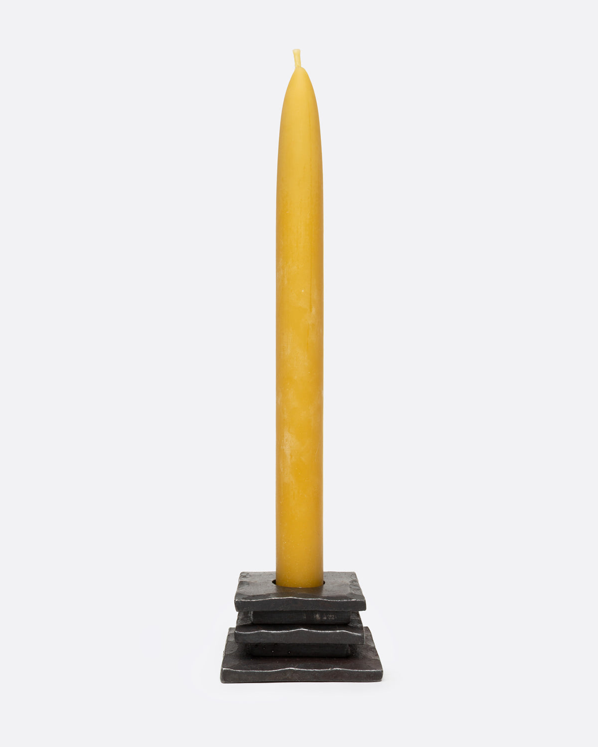 An iron stacked square candle holder with a hammered texture and a circular cutout in the top surface, shown with a candle in it from the front.