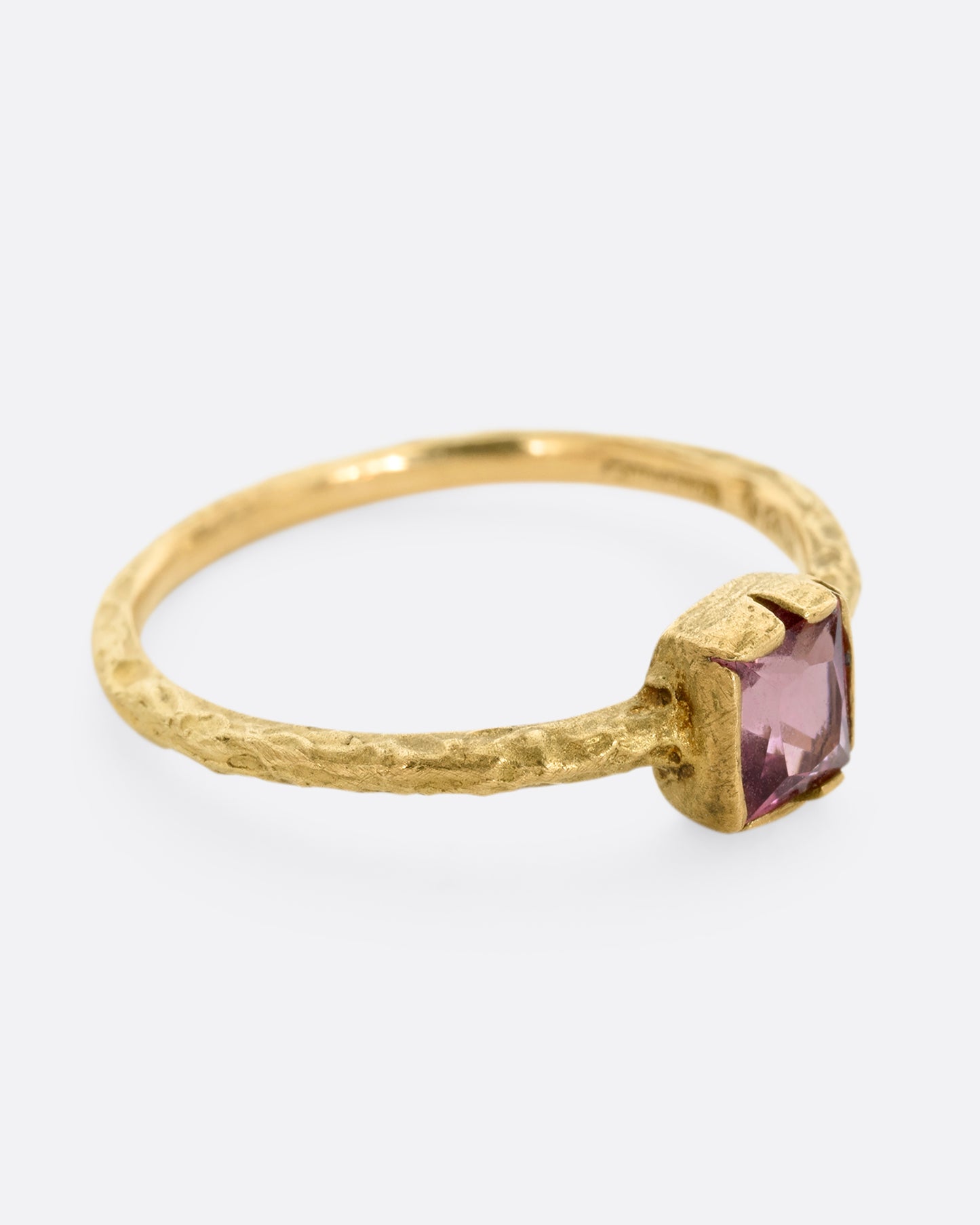 A textured yellow gold ring with a square pink tourmaline. Shown from the side.