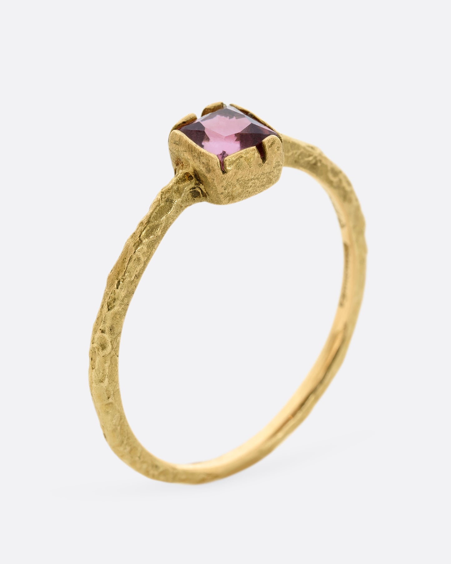 A textured yellow gold ring with a square pink tourmaline. Shown from the side, standing up.