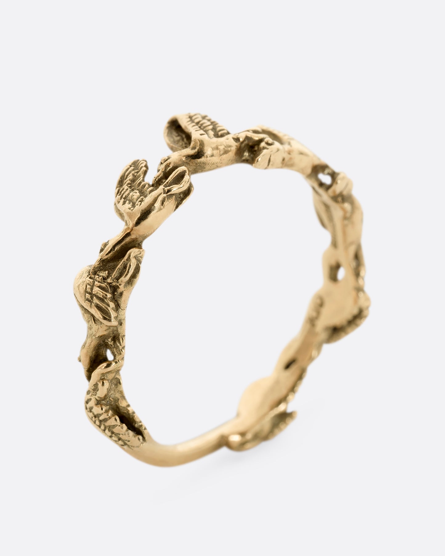 A yellow gold ring with birds flying around the majority of the band. Shown from the side, standing up.