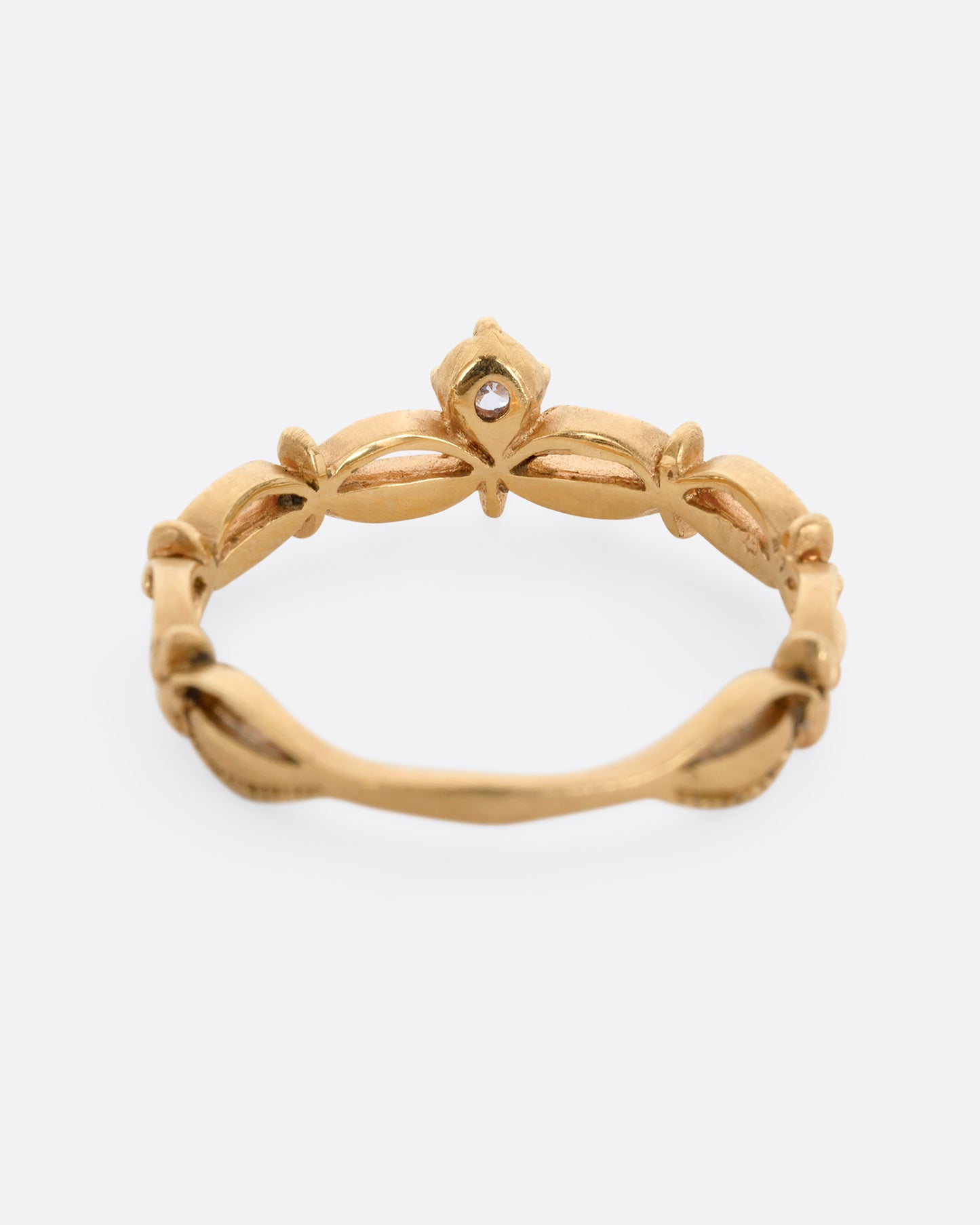 A yellow gold tiara shaped band with curved and textured details and a round white diamond at the center. Shown from the back.