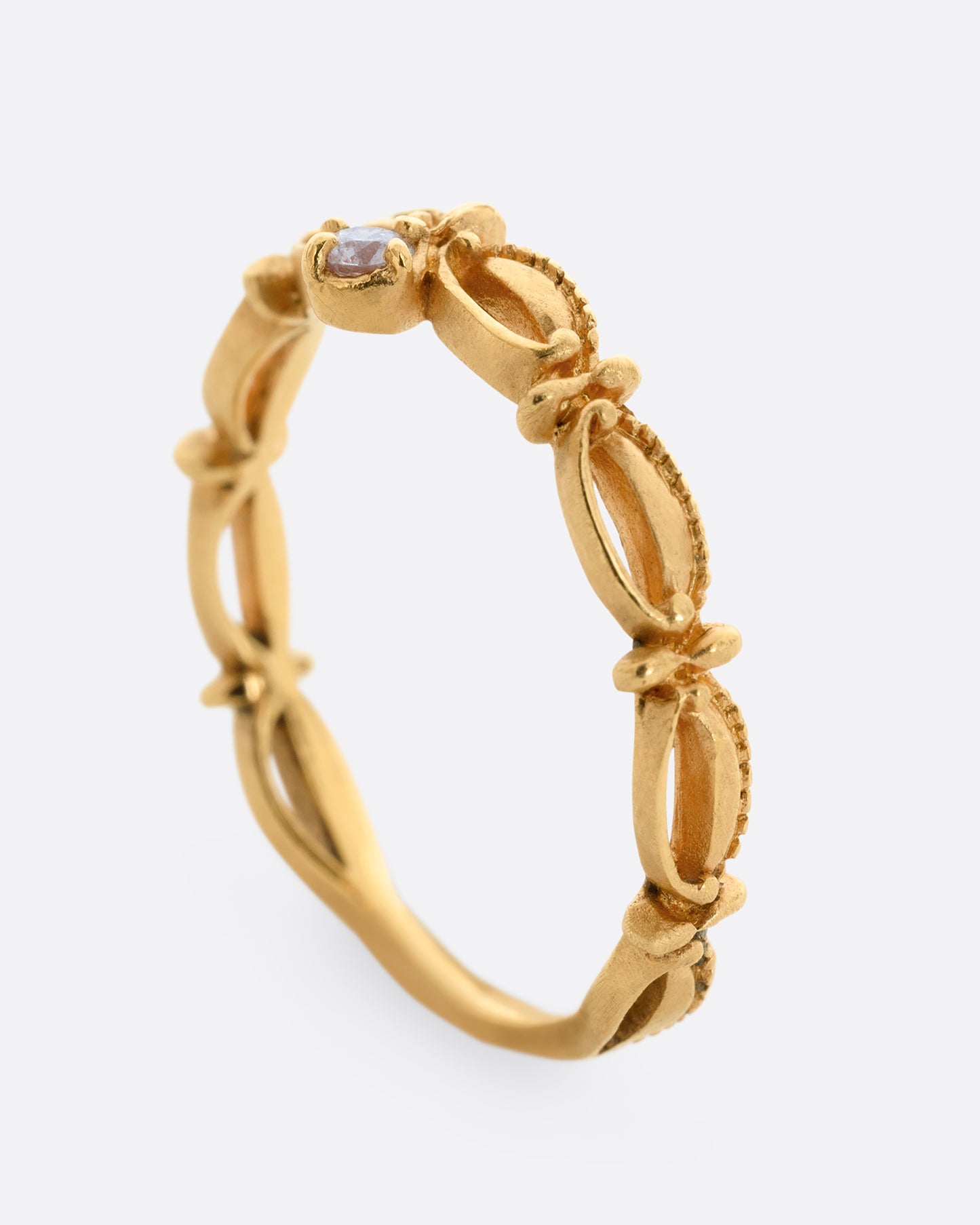 A yellow gold tiara shaped band with curved and textured details and a round white diamond at the center. Shown from the side, standing up.