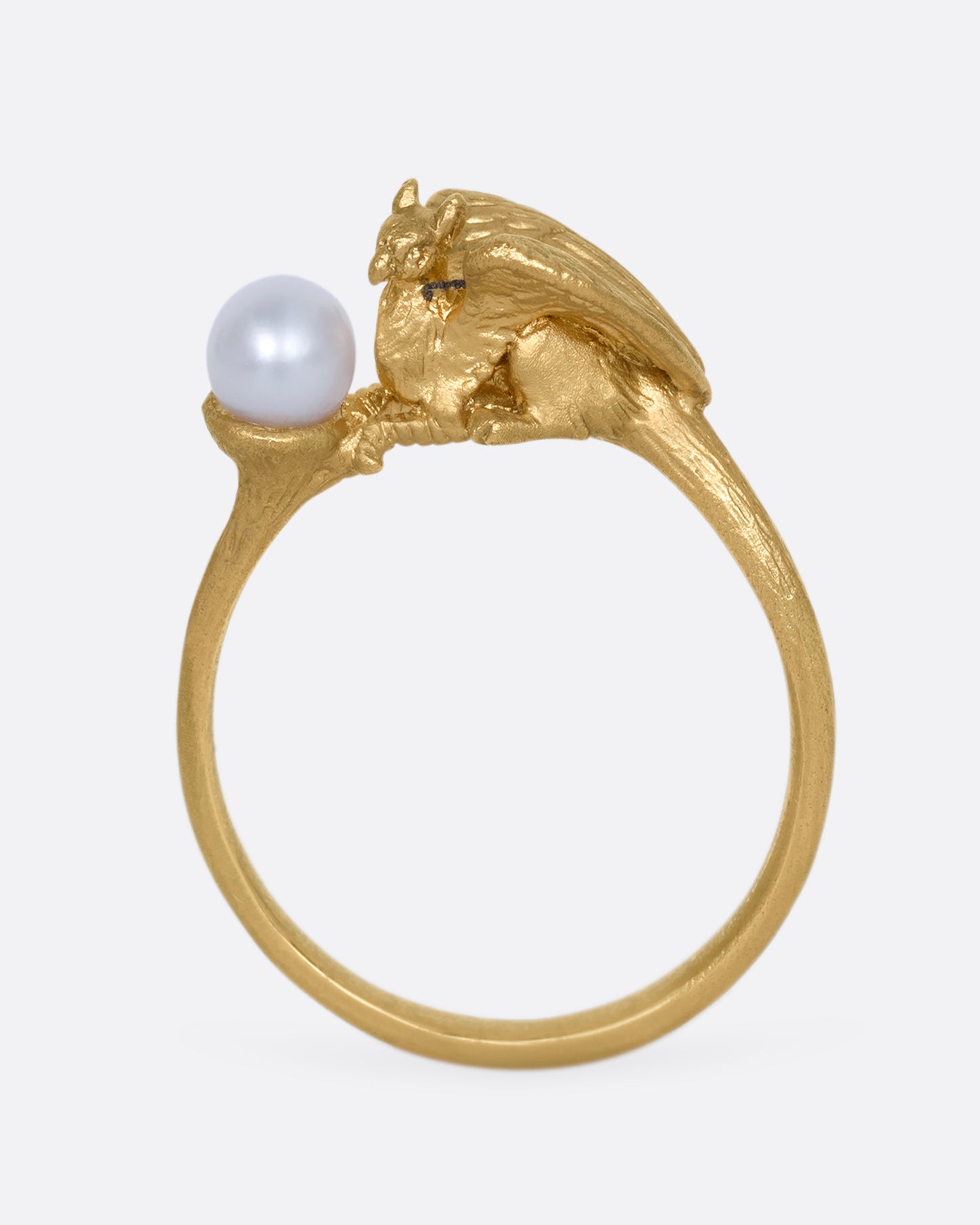 A yellow gold ring with a gryphon and a pearl. Shown standing up from the front.