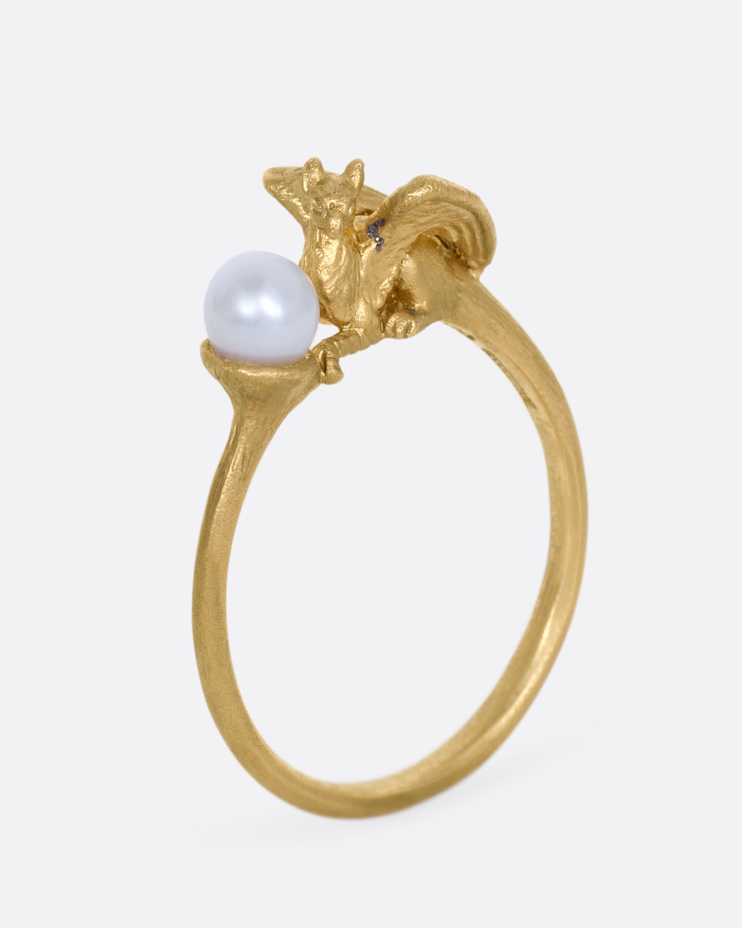 A yellow gold ring with a gryphon and a pearl. Shown standing up from the side.