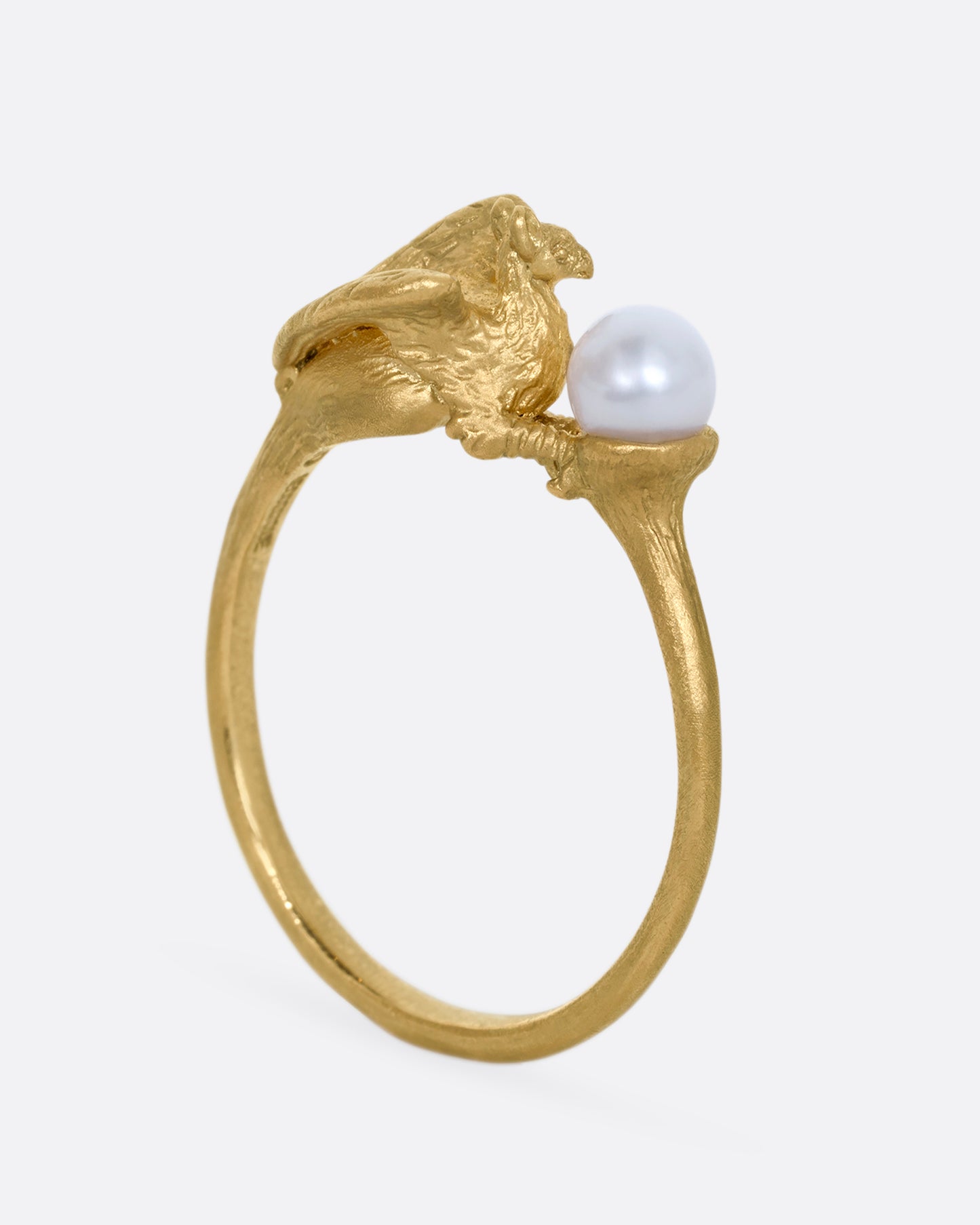 A yellow gold ring with a gryphon and a pearl. Shown standing up from the back.