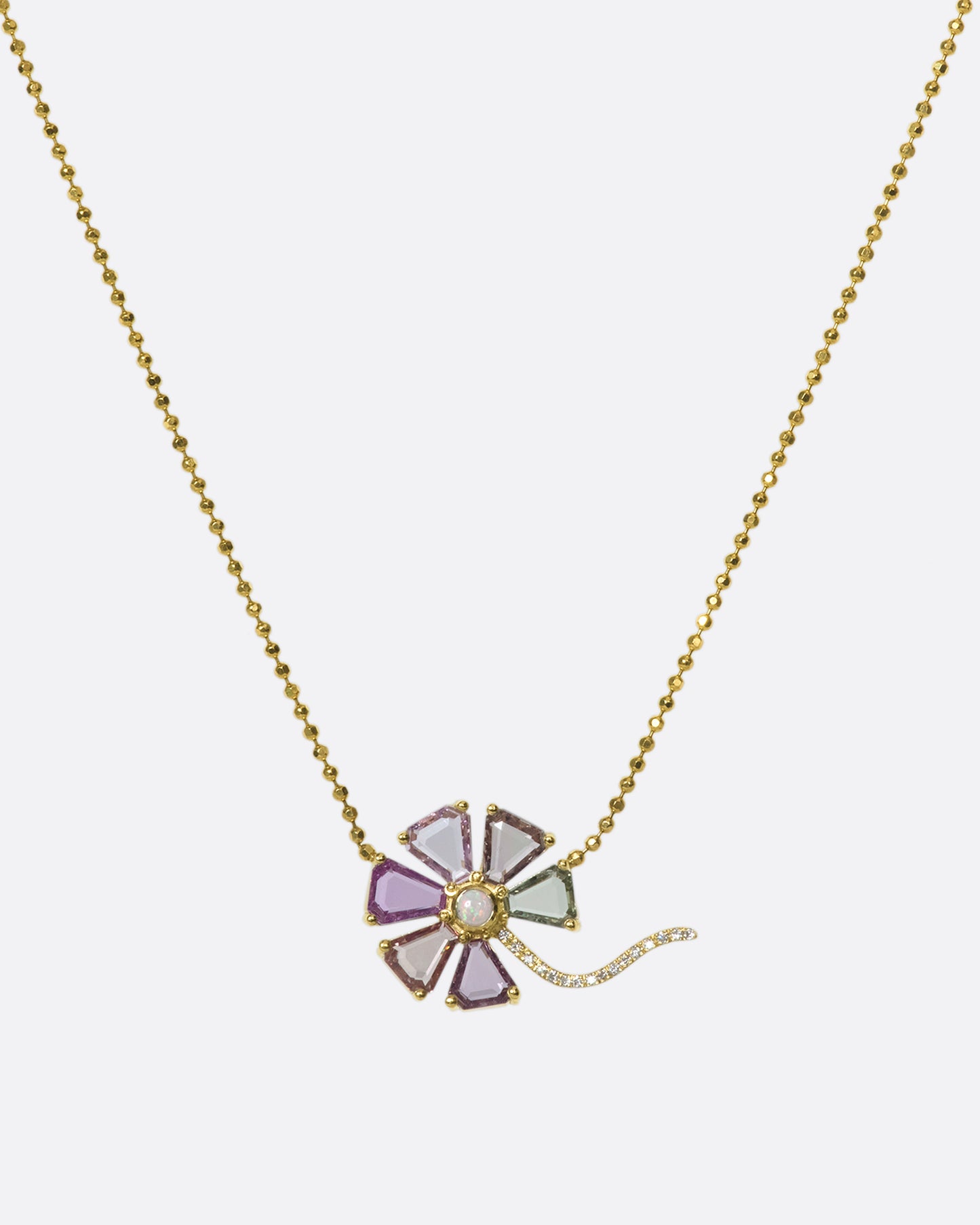 A zoomed out view of a flower pendant with sapphire petals, diamond stem, and opal center on a gold ball chain.