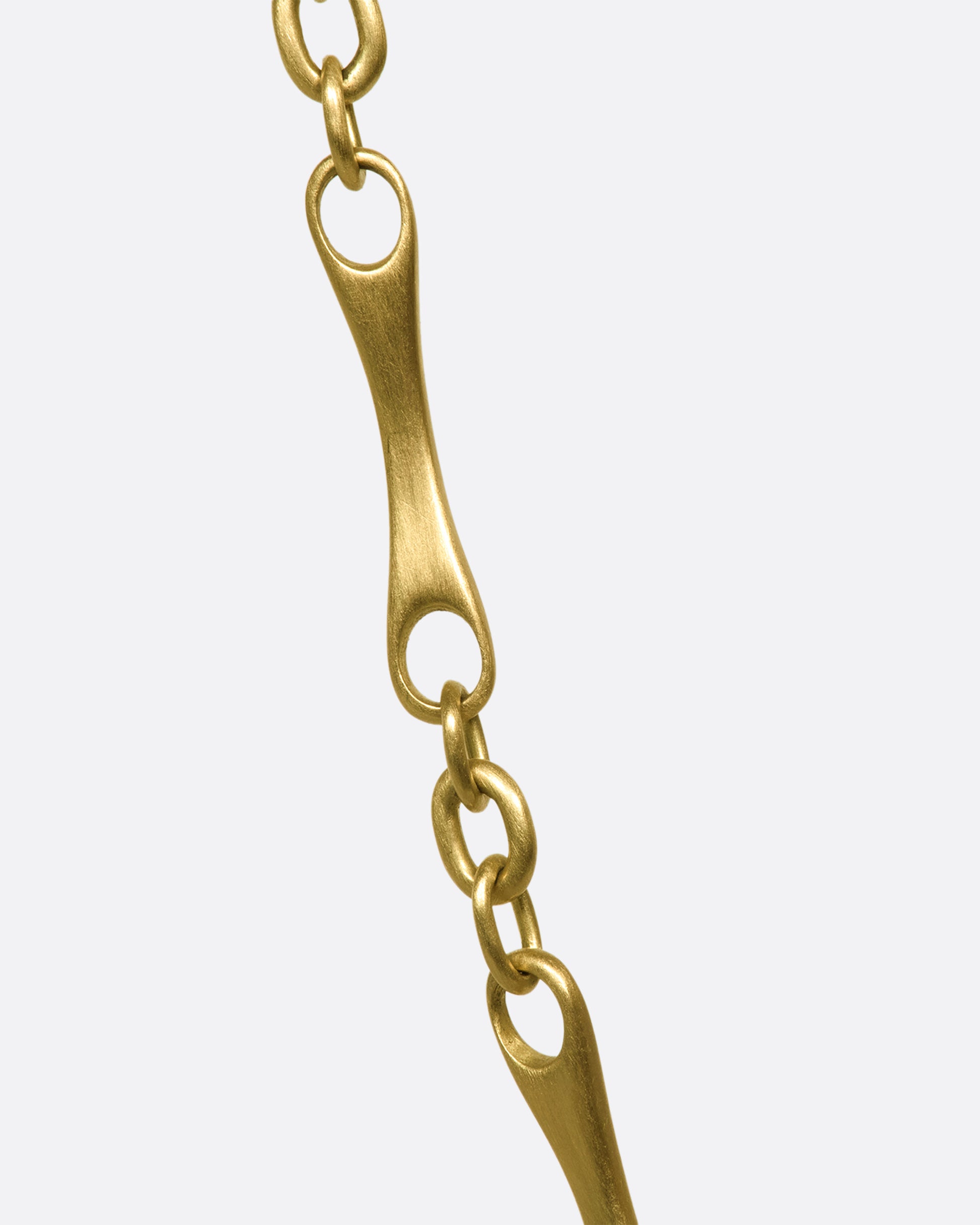 A close up of a gold necklace with elongated links with circular cut outs on each end.