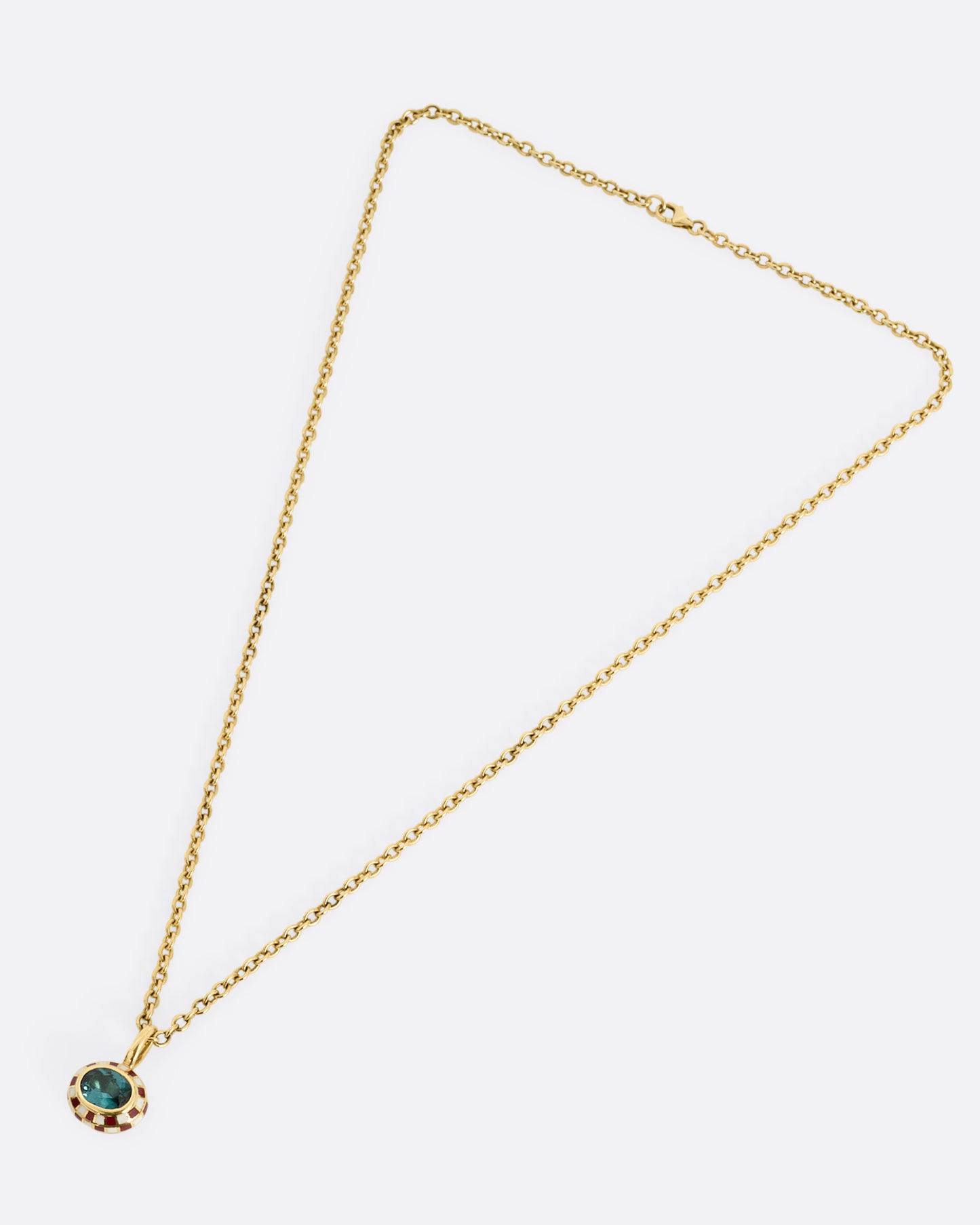 A yellow gold cable chain necklace with a red and cream enamel checkerboard pendant around a green tourmaline. The reverse side of the pendant has a checked pattern. Shown from the front.