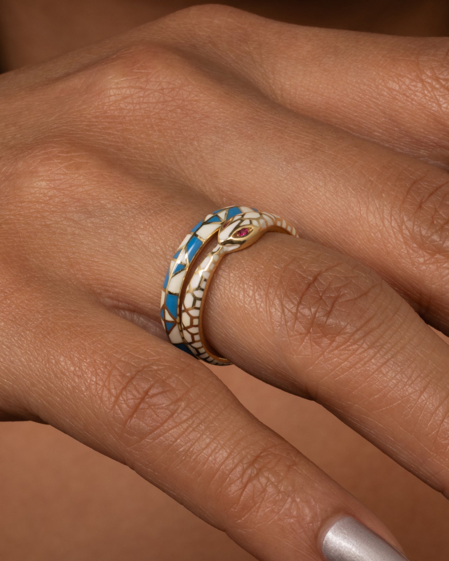 A yellow gold band ring with a turquoise and cream enamel patchwork pattern. Shown worn.