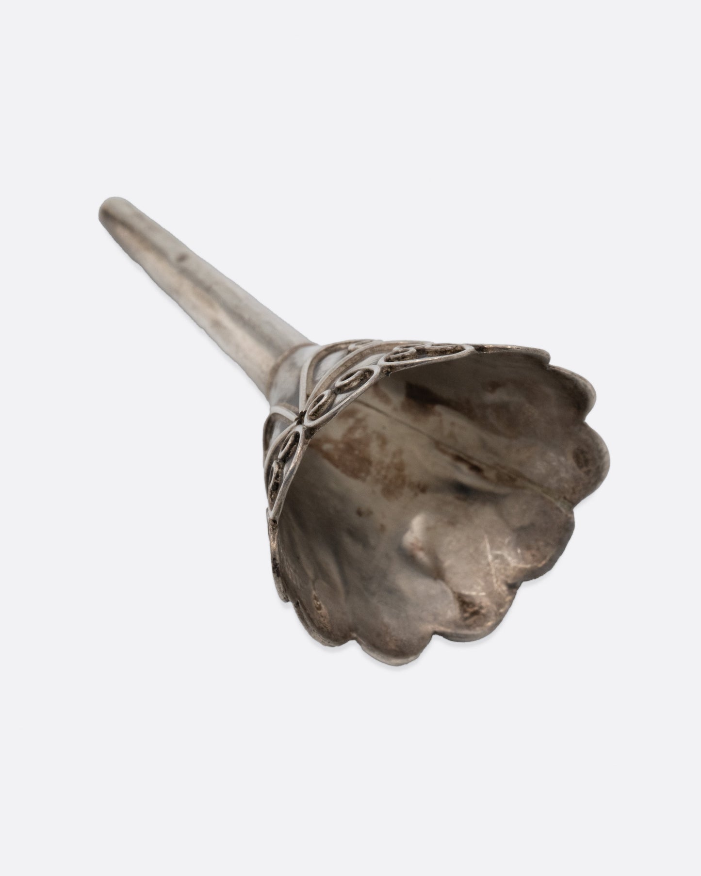A small silver funnel with decorative scroll work at the top. Shown on its side from the top.