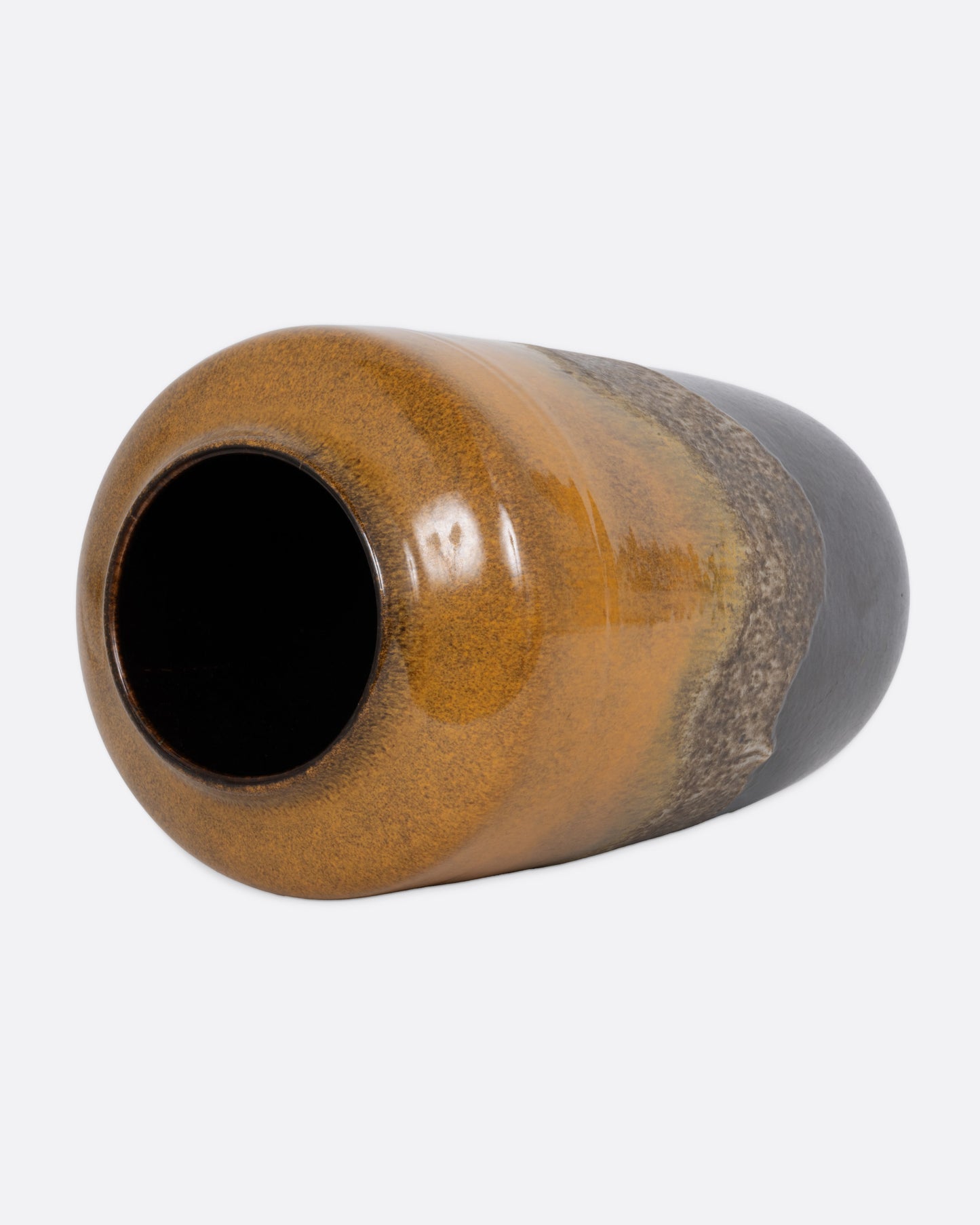 A tall ceramic vase with a ochre- to- brown gradient glaze, shown lying on its side from the top.
