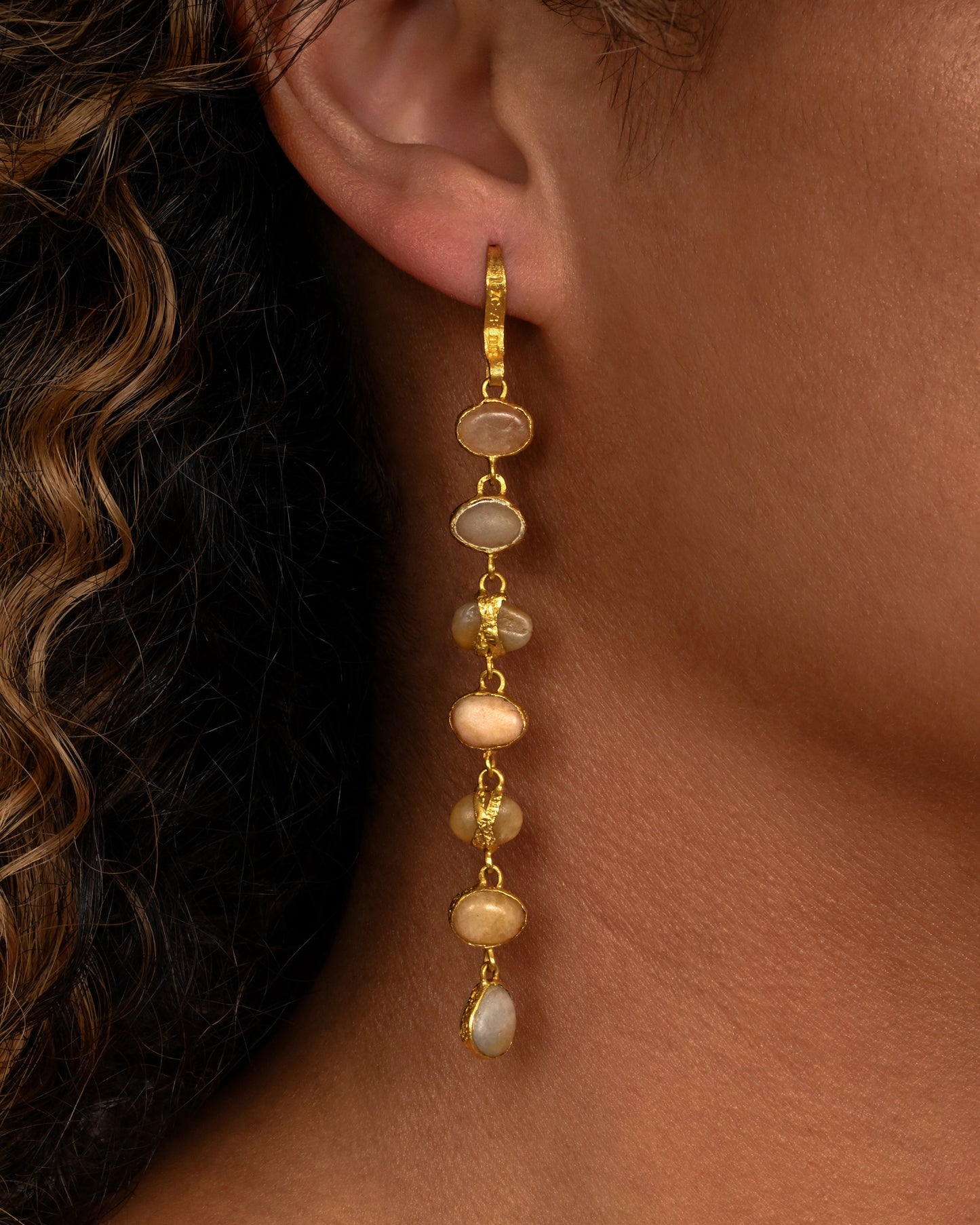 Seven river pebbles, each wrapped in yellow gold hanging from a yellow gold ear hook. Shown from the front on a person.