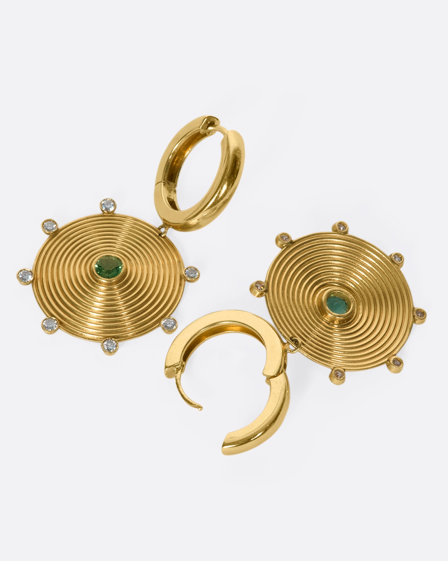 A pair of 14k gold hoops with gold disc drops, dotted with diamonds and emeralds. The discs' ribbed pattern constantly catches the light, giving the illusion of two glowing suns.