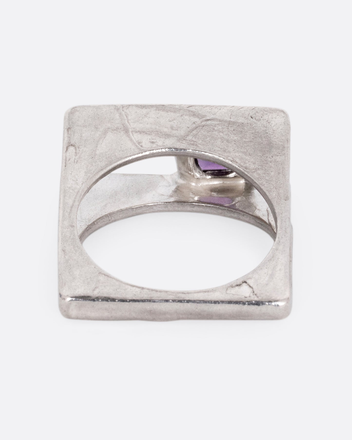 A silver square ring that widens to reveal a princess cut amethyst, shown from the back.