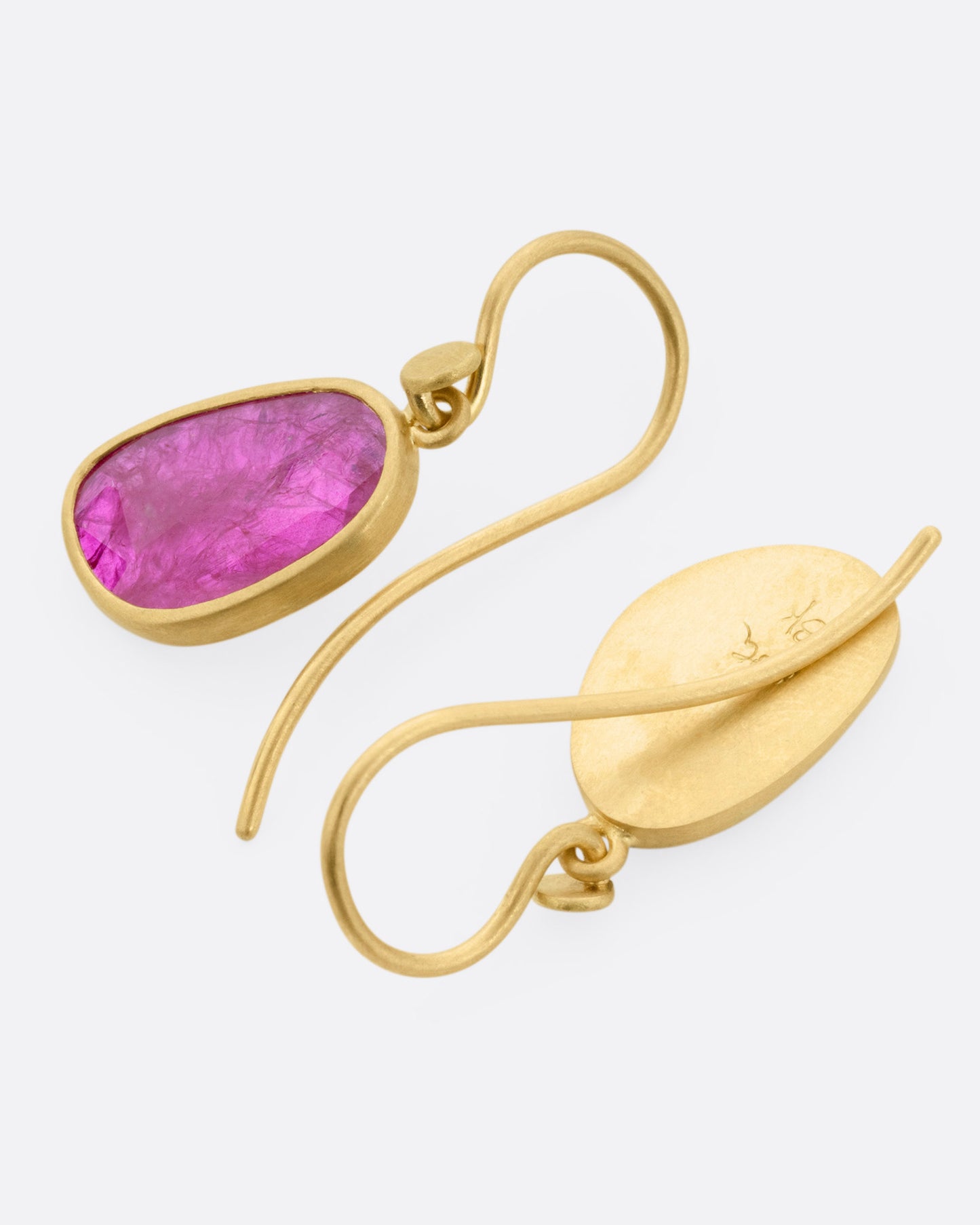 A pair of yellow gold drop earrings with Mozambique rubies, shown lying flat with one earring facing front and the other back.