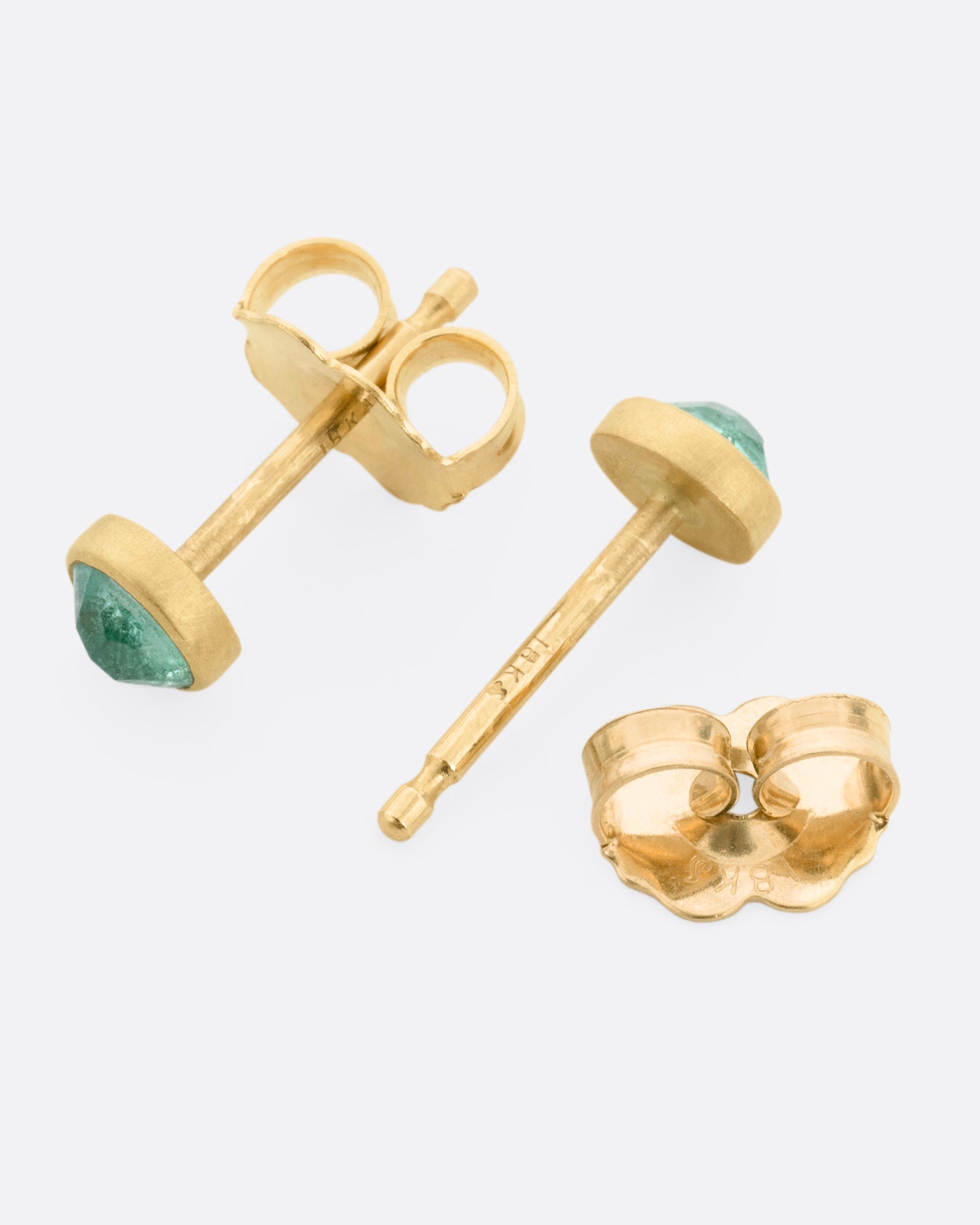 A pair of yellow gold stud earrings with Colombian emeralds, shown lying on their sides with one earring open.