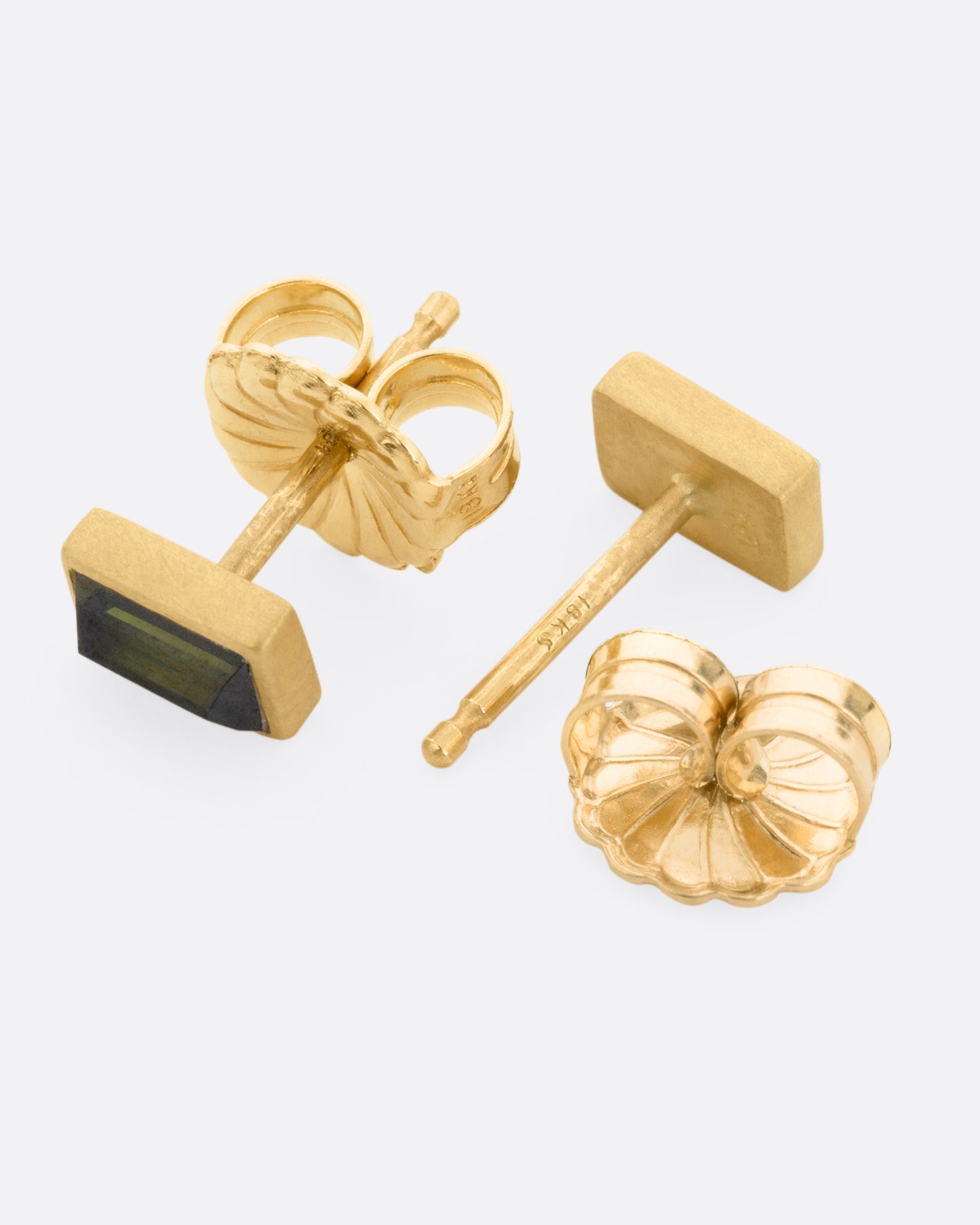 A pair of yellow gold green tourmaline baguette earrings, shown lying on their sides with one earring open.