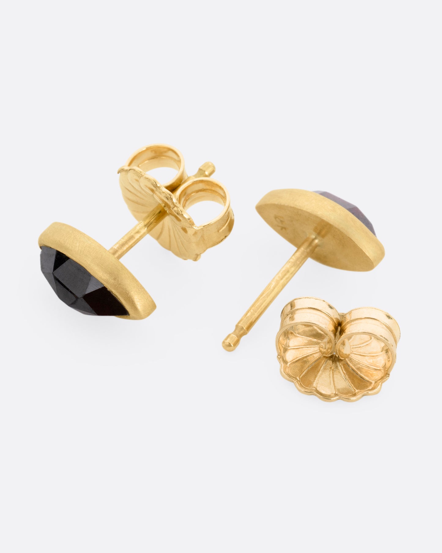 A pair of yellow gold navette garnet earrings, shown lying on their sides with one earring open.