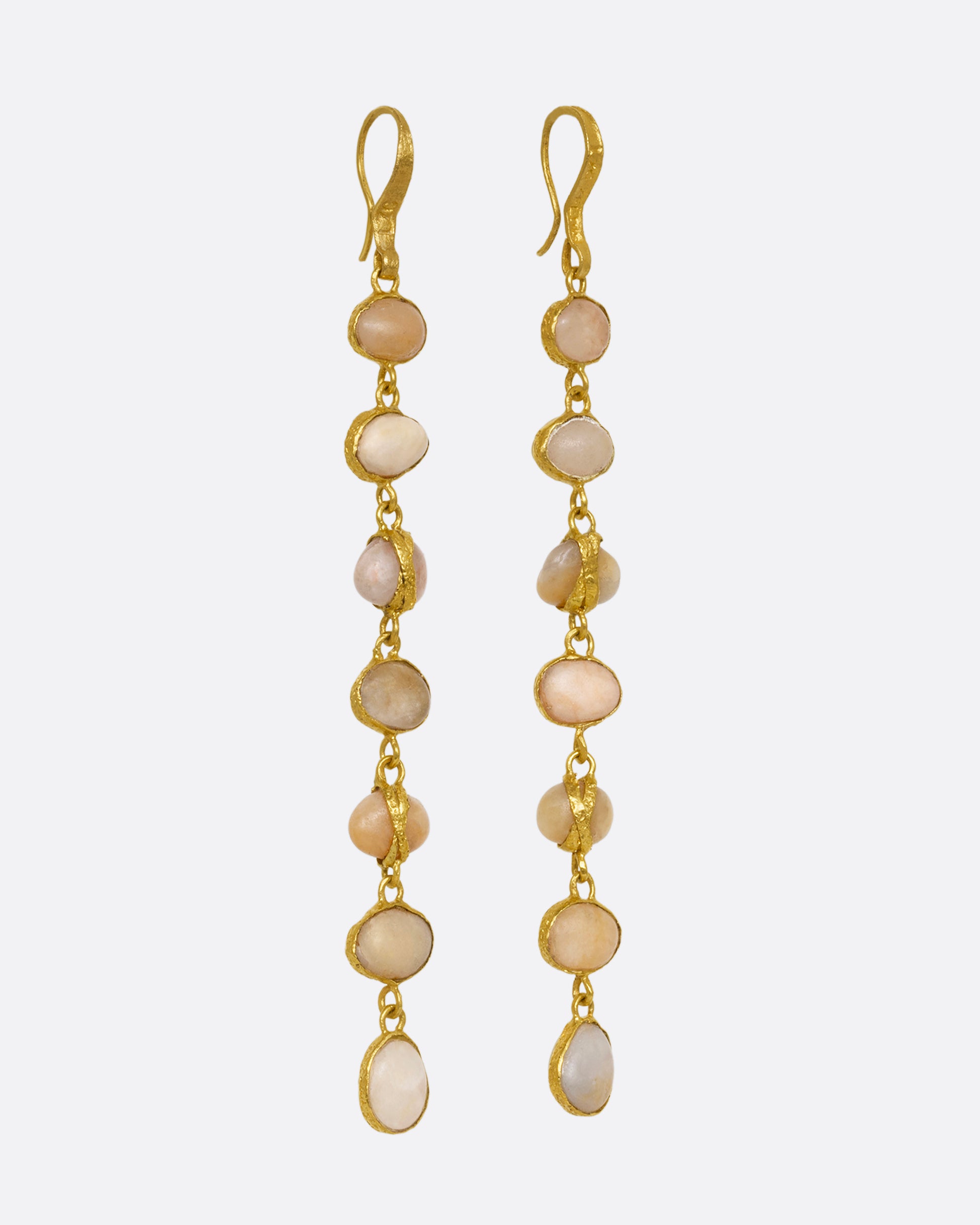 A pair of earrings with even river pebbles, each wrapped in yellow gold hanging from yellow gold ear wires. Shown from the side.