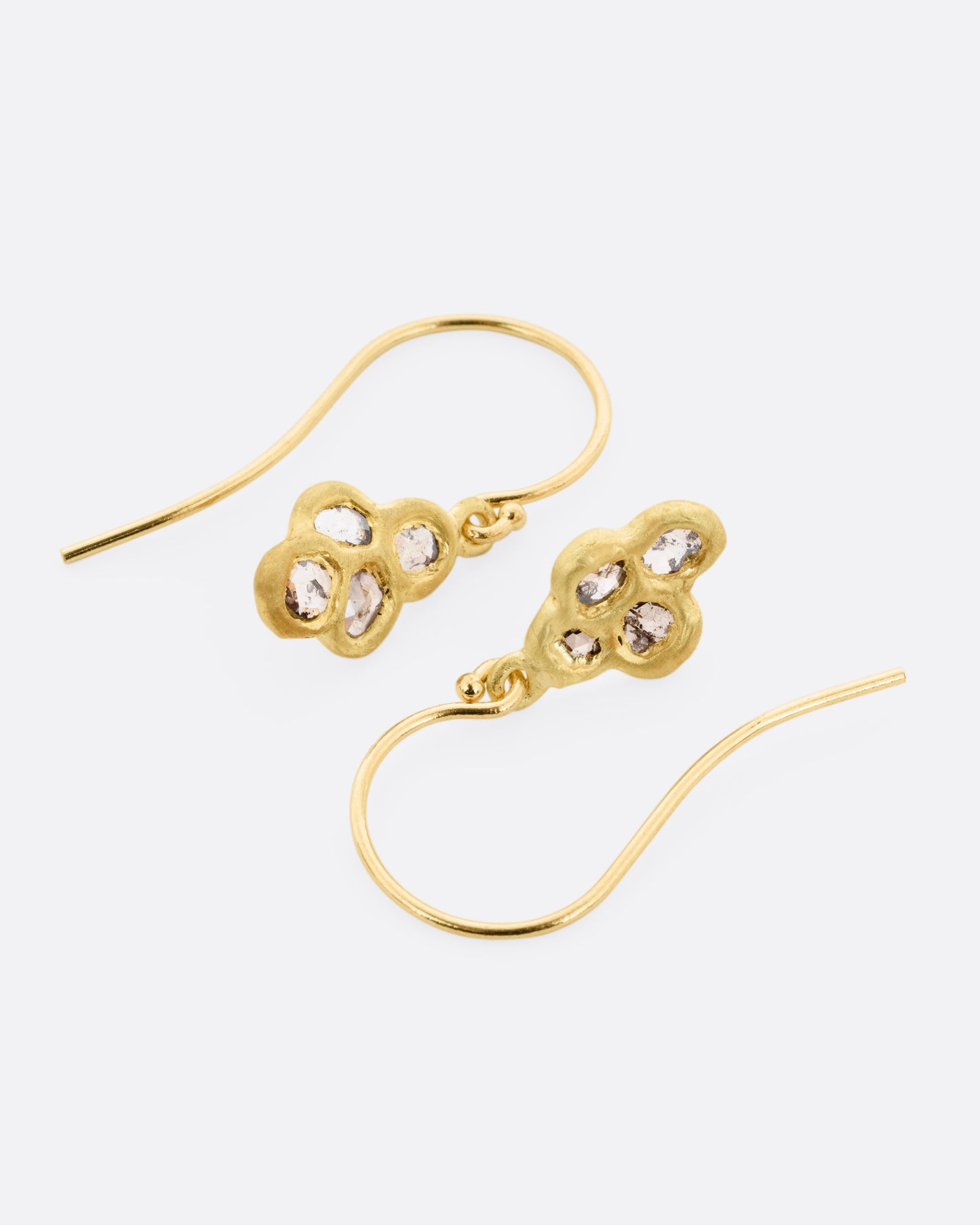 A pair of yellow gold drop earrings with four rose cut diamonds, shown lying on their sides.