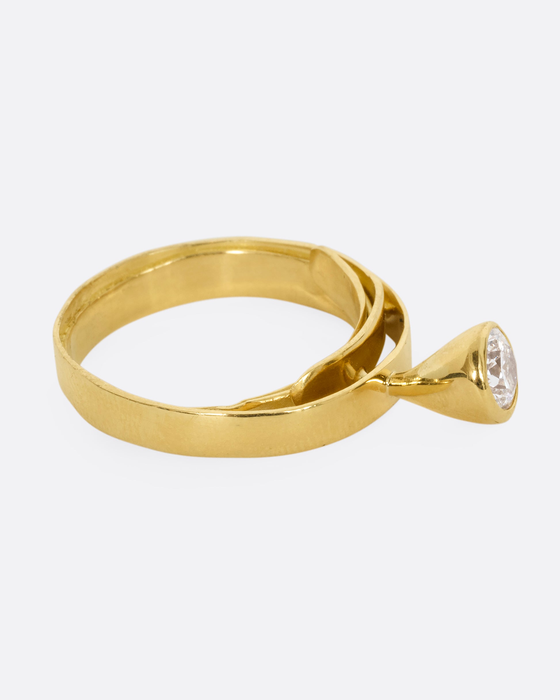 A yellow gold ring that loops over itself twice with a tall bezel set diamond at its center. Shown from the side.