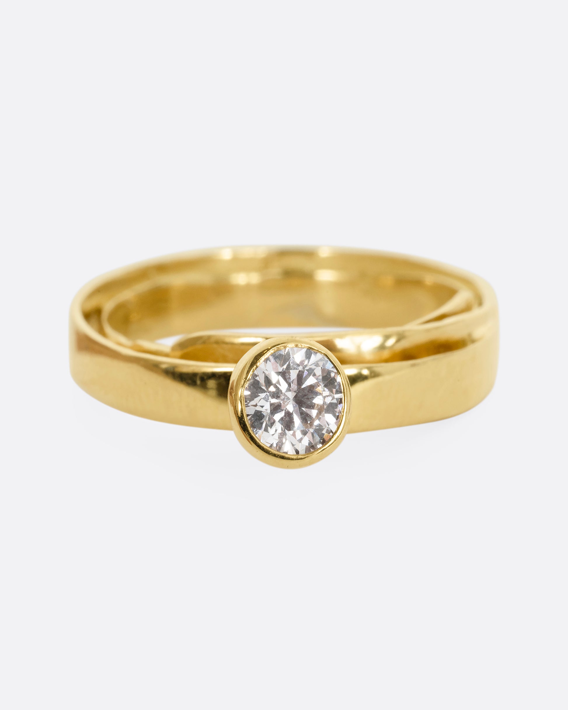 A yellow gold ring that loops over itself twice with a tall bezel set diamond at its center. Shown from the top.