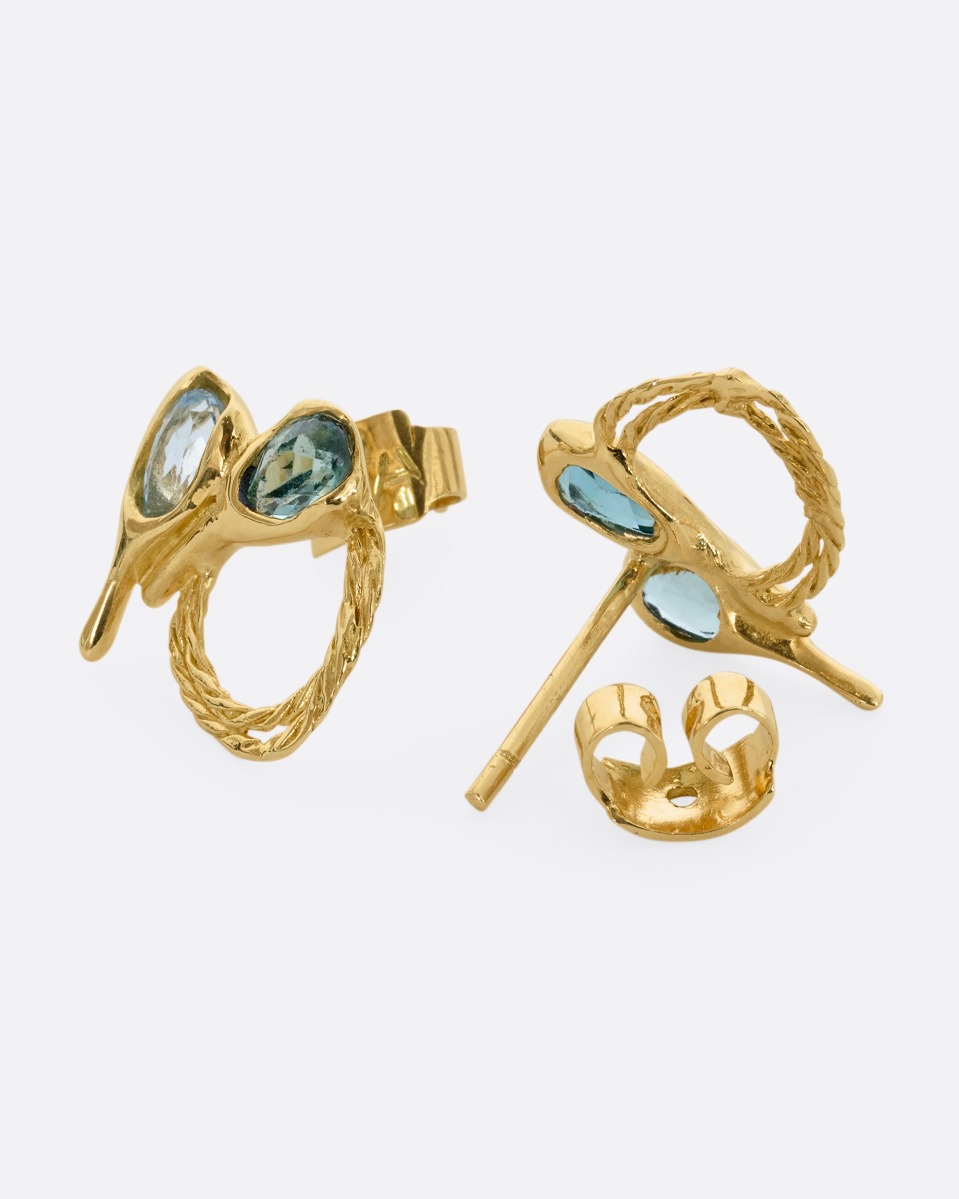 A pair of yellow gold stud earrings with two free- form blue green tourmalines and textural hoops. One earring is shown on its side from the front. The other is shown open on its side from the back.