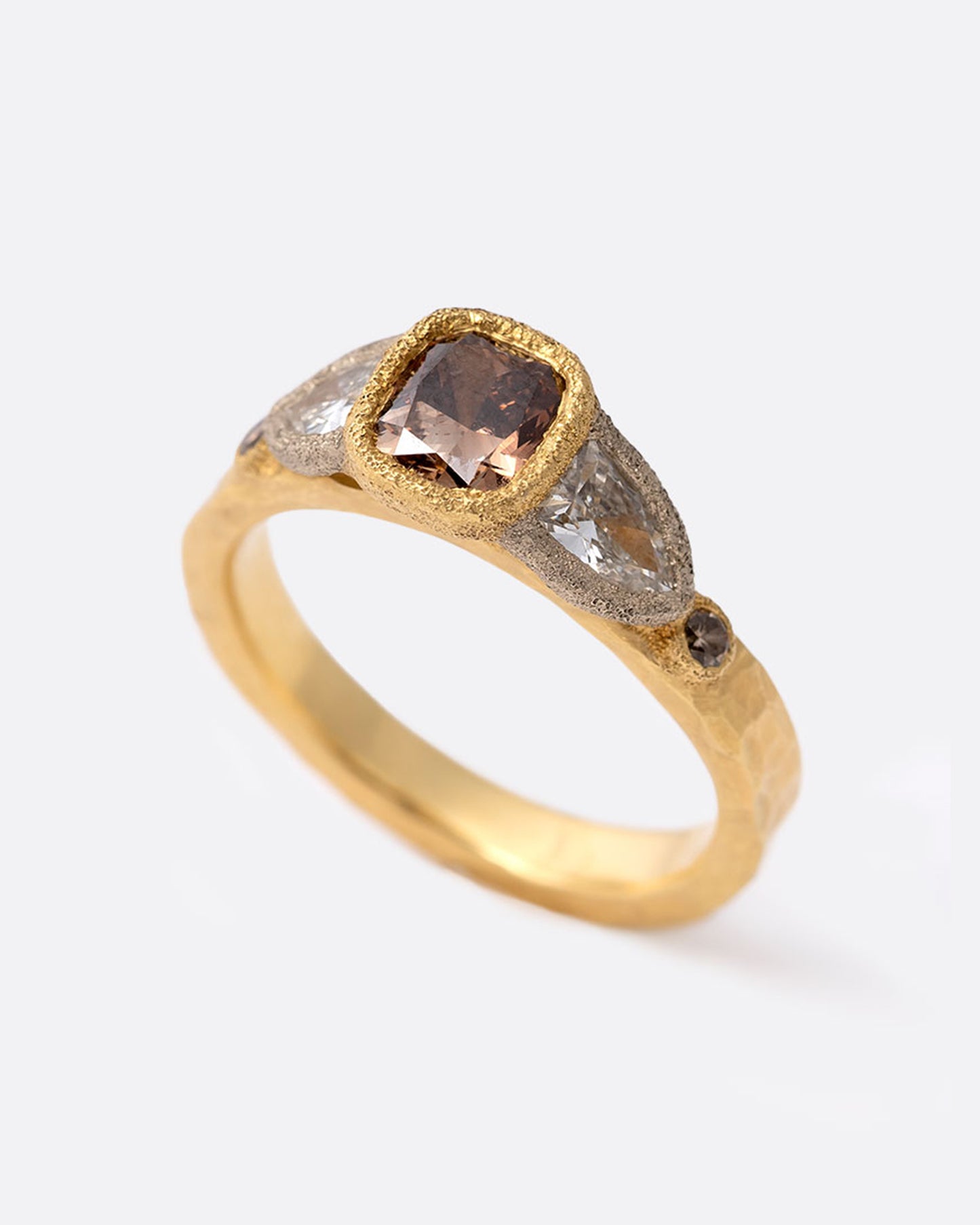 A yellow gold ring with a cushion cut cognac diamond at the center flanked by two shield cut diamonds and two smaller round cognac diamonds. Shown standing up at an angle from the front.