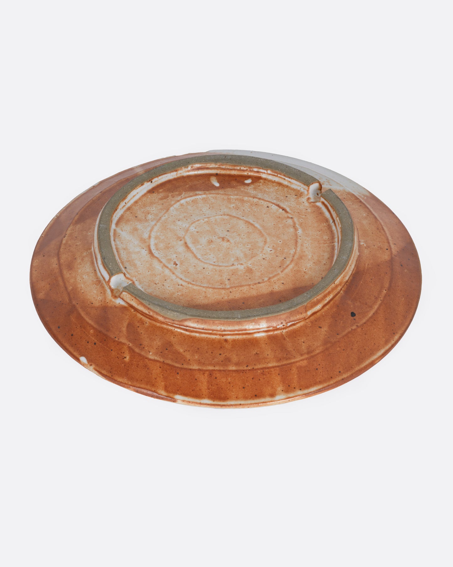 A ceramic plate with a hand painted abstract figure and an umber and white wash of color. Shown from the bottom.