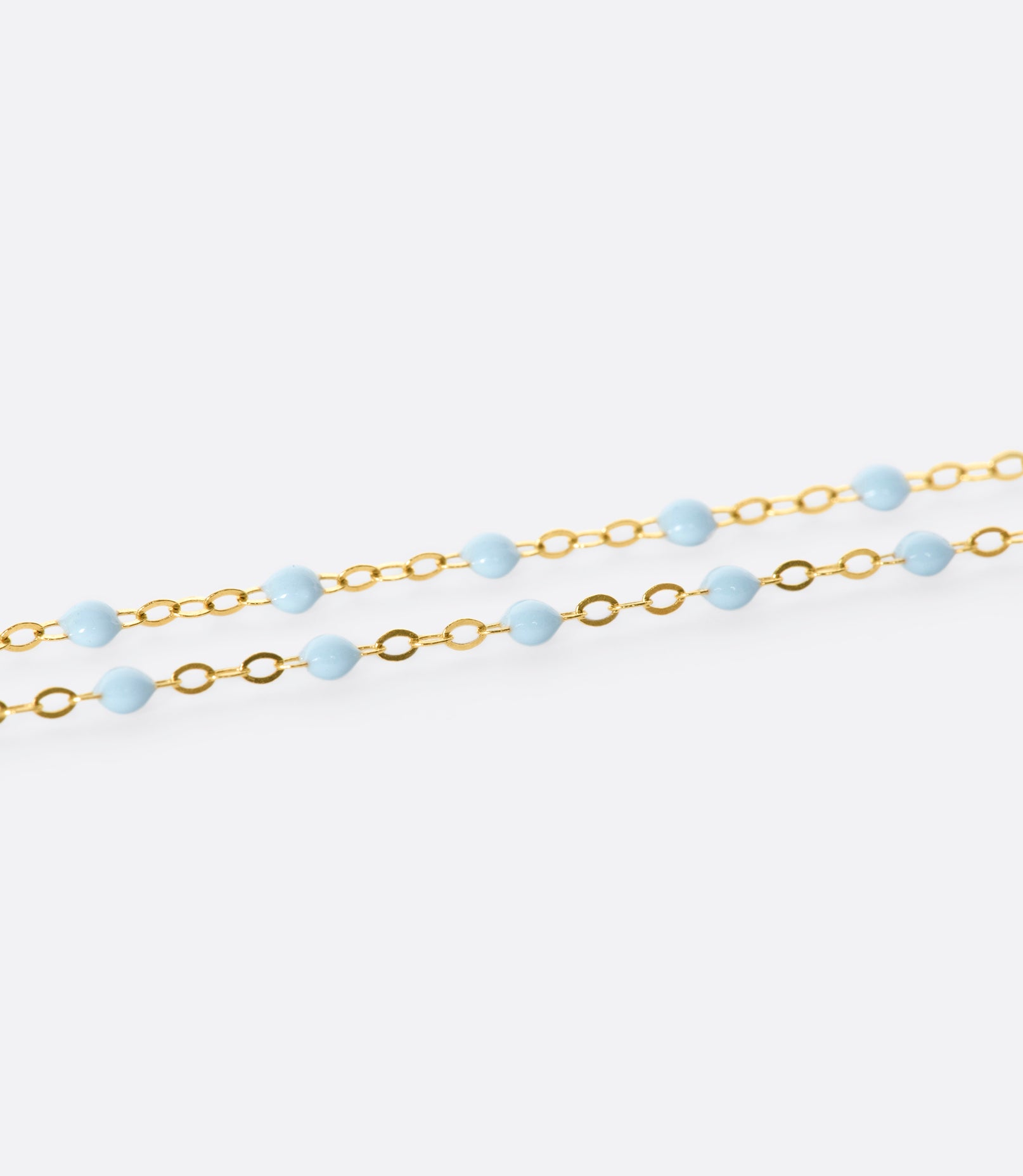A close up view of a yellow gold cable chain bracelet with baby blue resin droplets.
