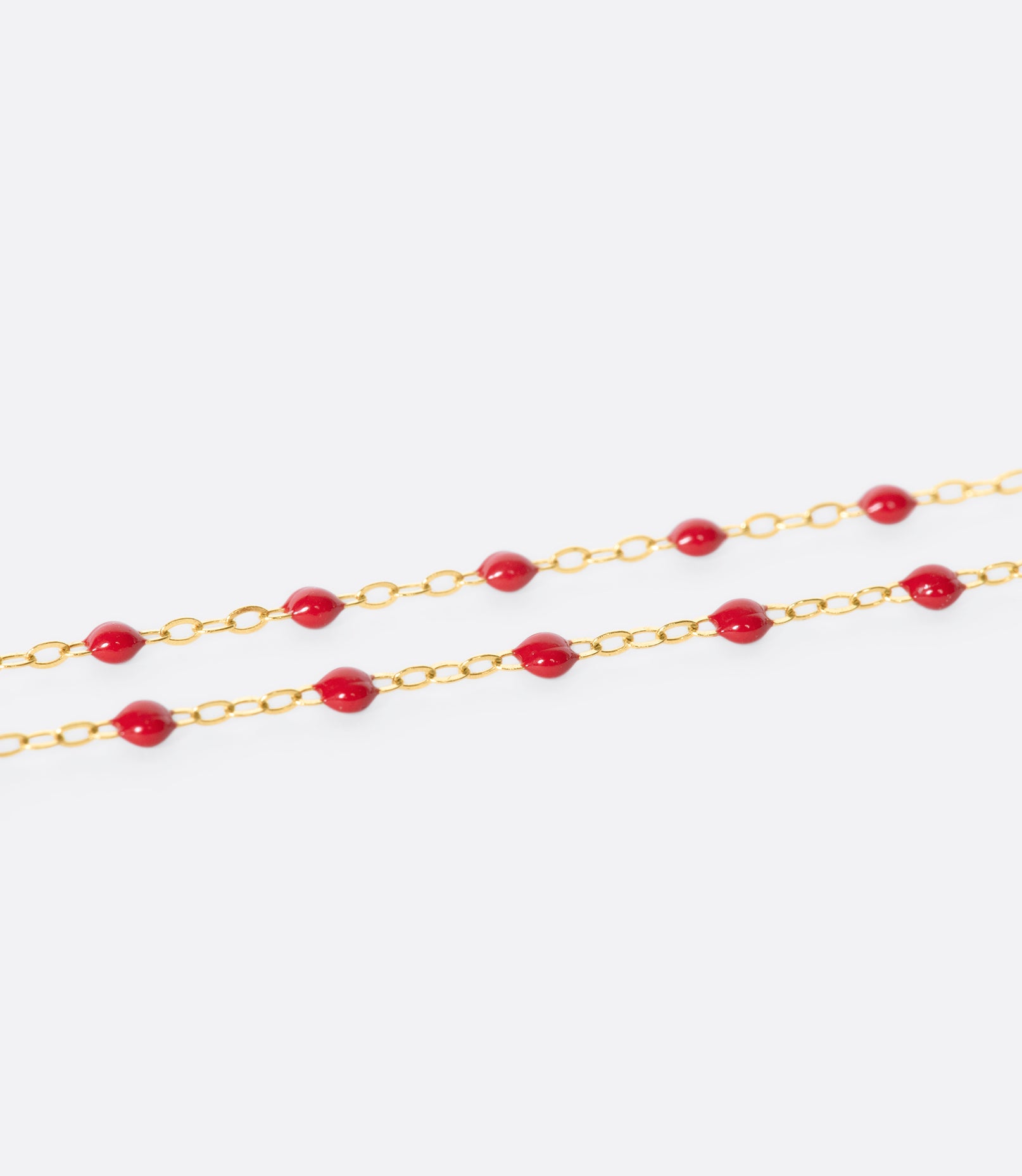 A close up view of a yellow gold cable chain bracelet with red resin droplets.