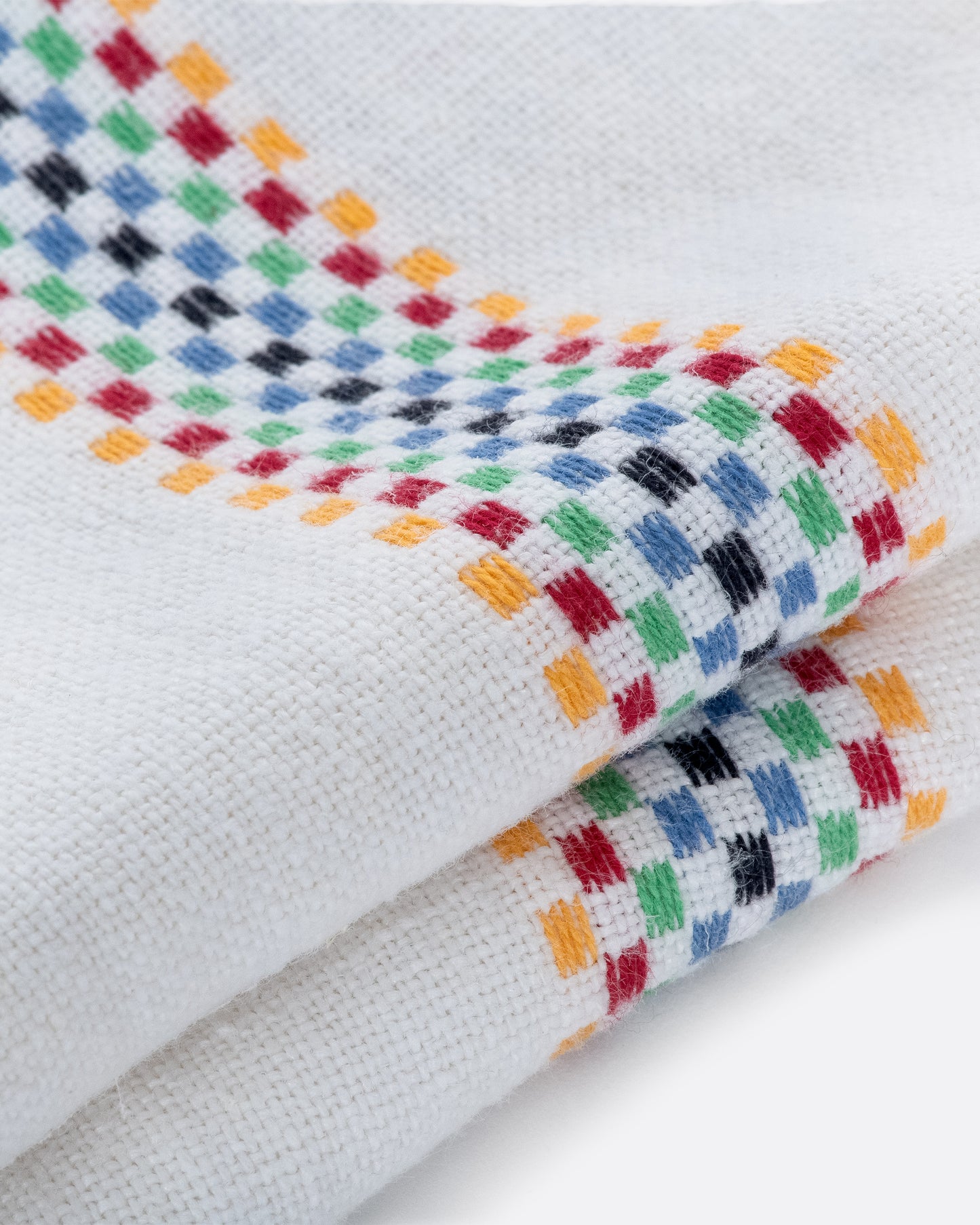 A white linen napkin with rainbow checkered embroidered stripes