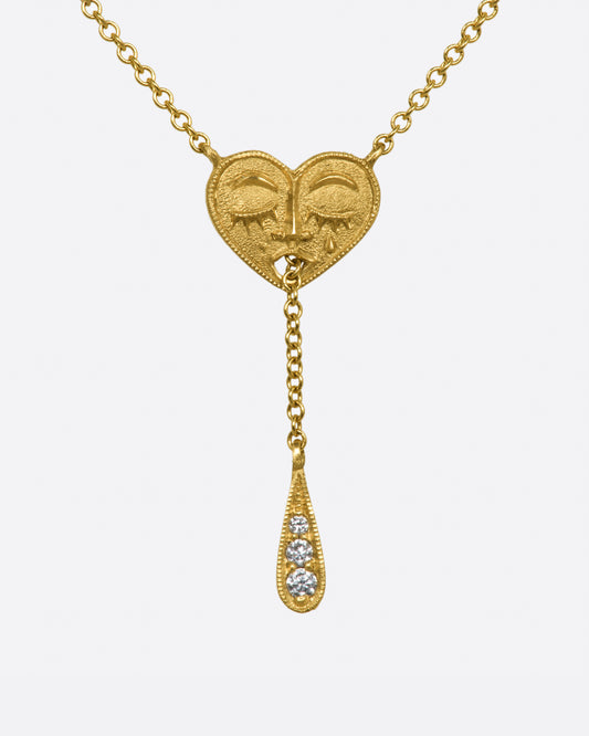 A yellow gold lariat necklace with a sleeping heart at its center, the chain comes through its mouth, and is weighed by a diamond teardrop.