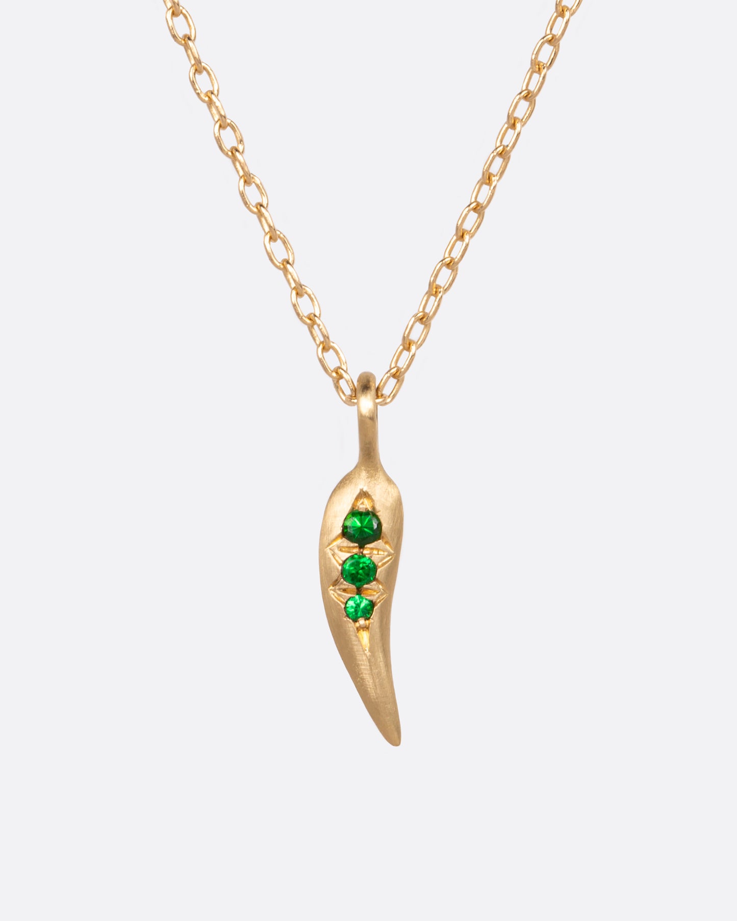 A yellow gold cable chain with a chili pepper shaped pendant with three vibrant green tsavorite garnets. Shown from the front.